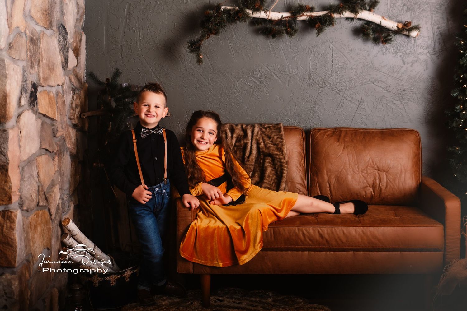 Two children in festive attire sitting on a brown leather couch with holiday decorations.