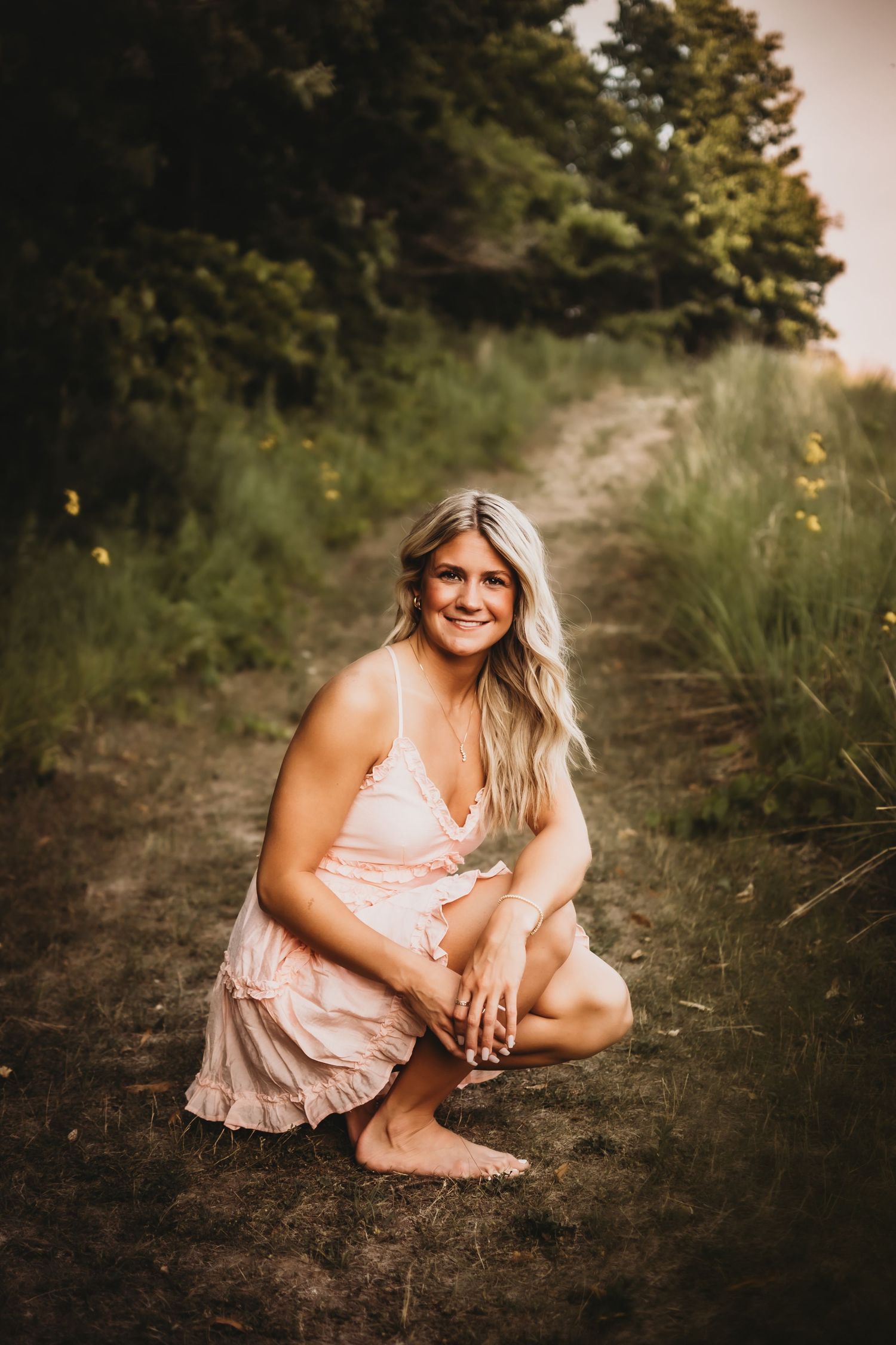 Person wearing pink dress poses on a rustic trail with wildflowers.