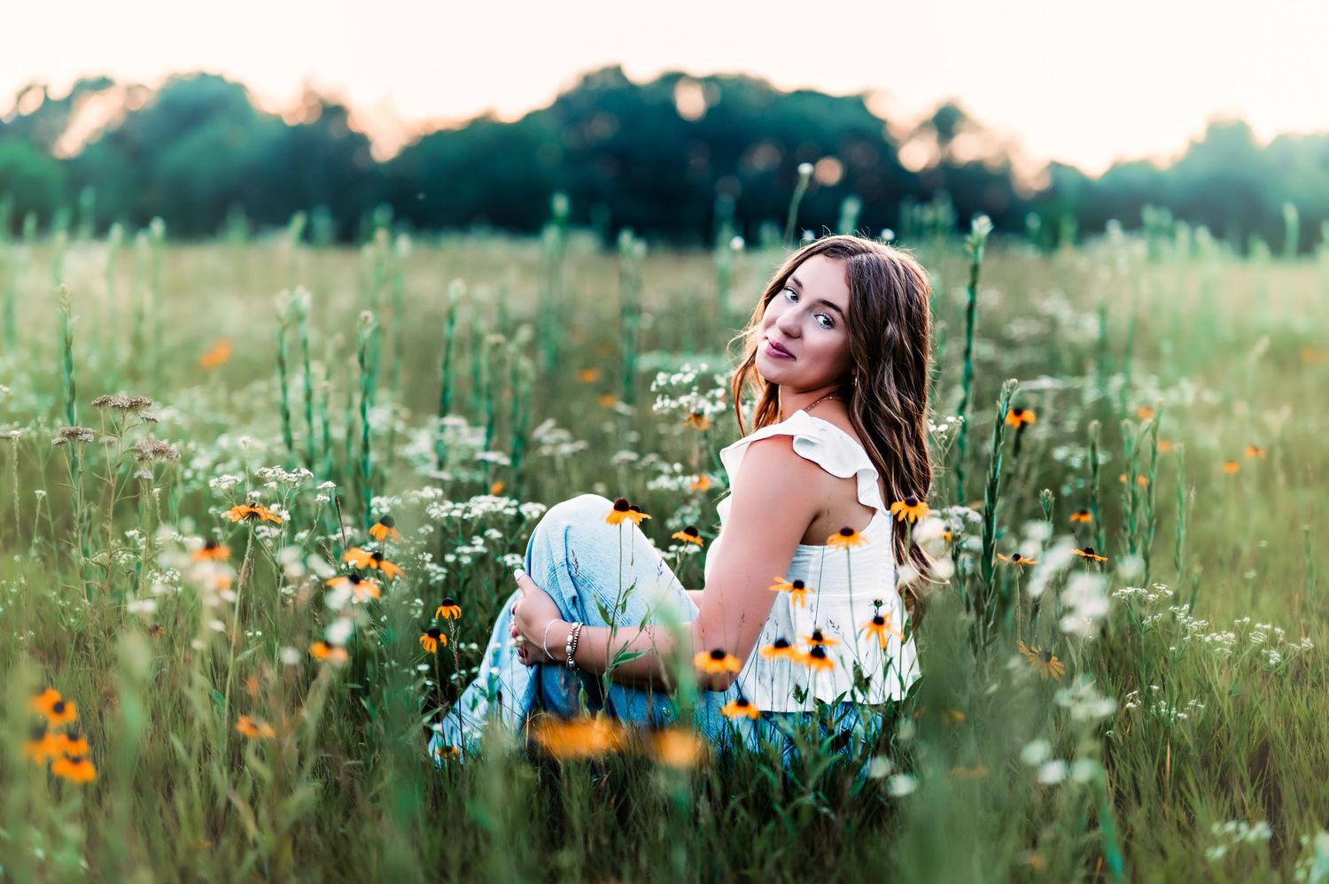 A person lies in a field of blooming white daisies and yellow wildflowers during golden hour in Grafton, WI