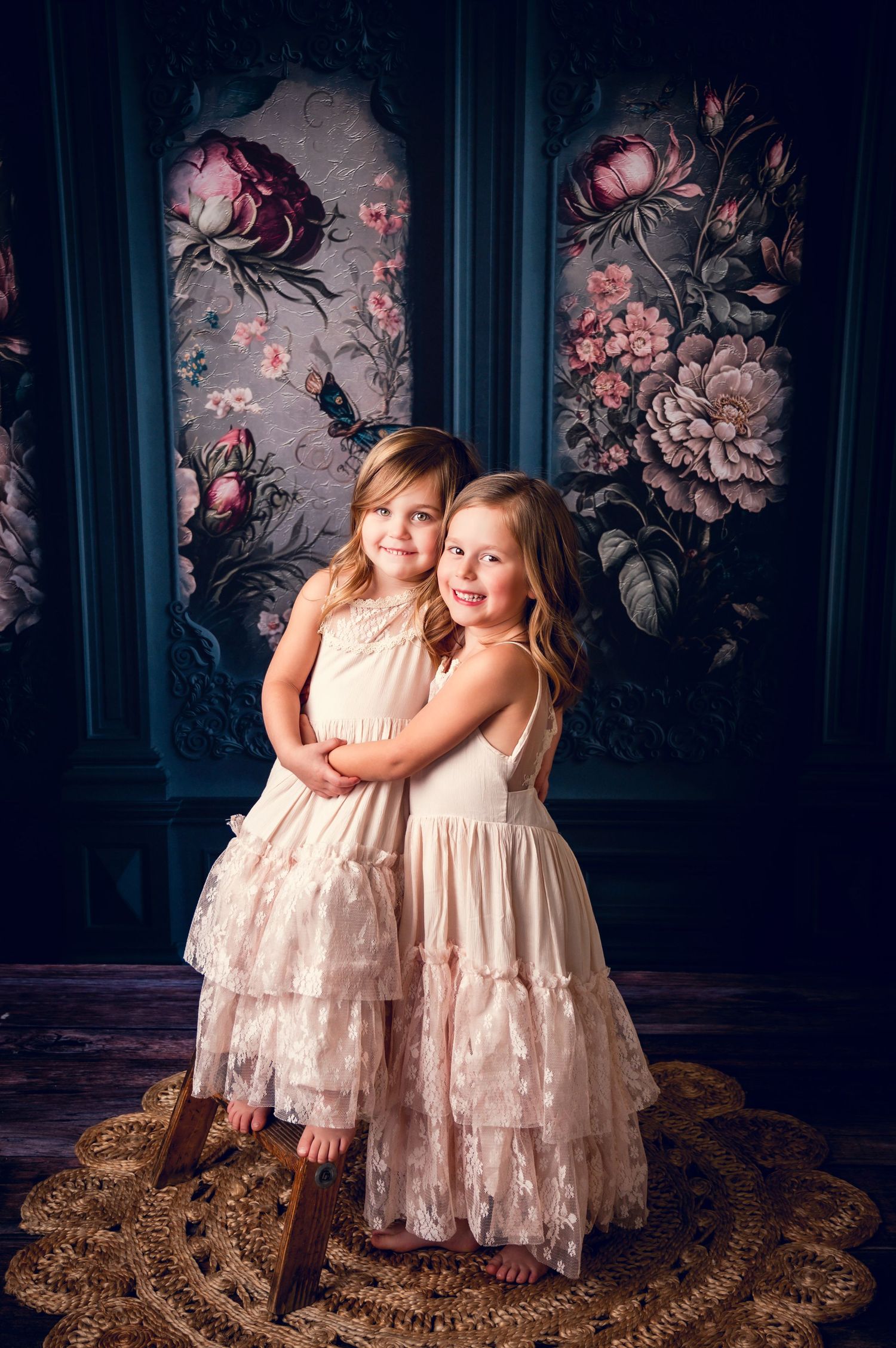 Two cream lace dresses photographed against dark floral wallpaper in vintage style.