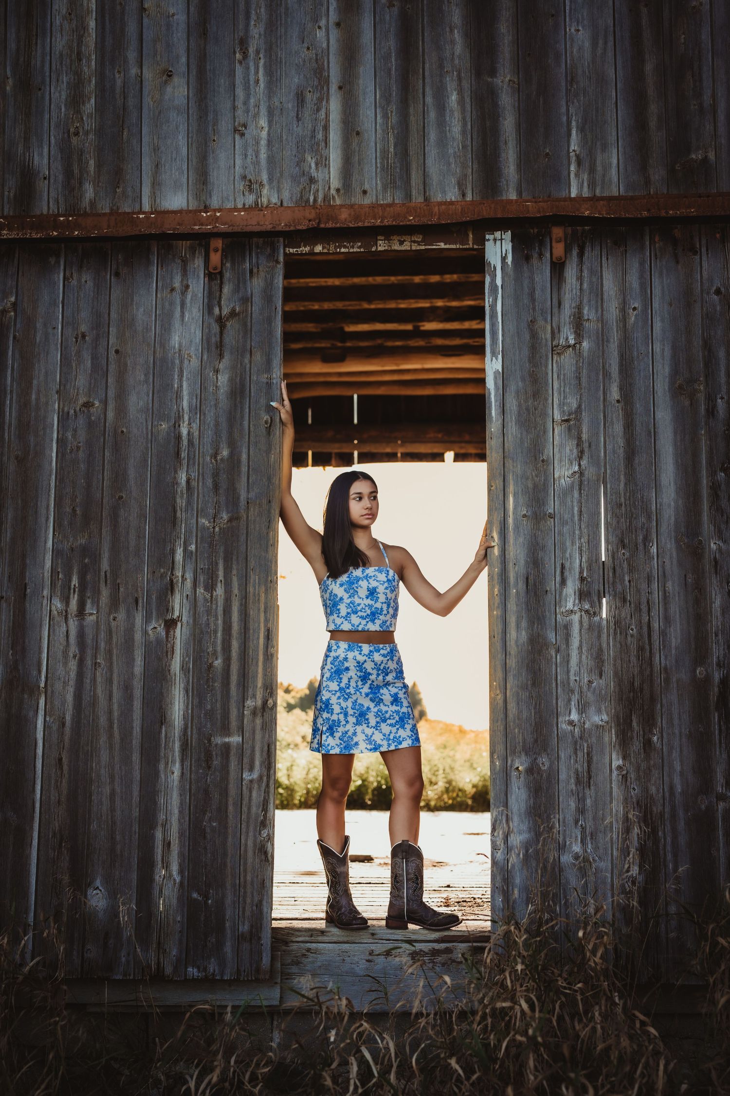 Fashion photo in doorway of rustic barn with model in blue dress and boots.