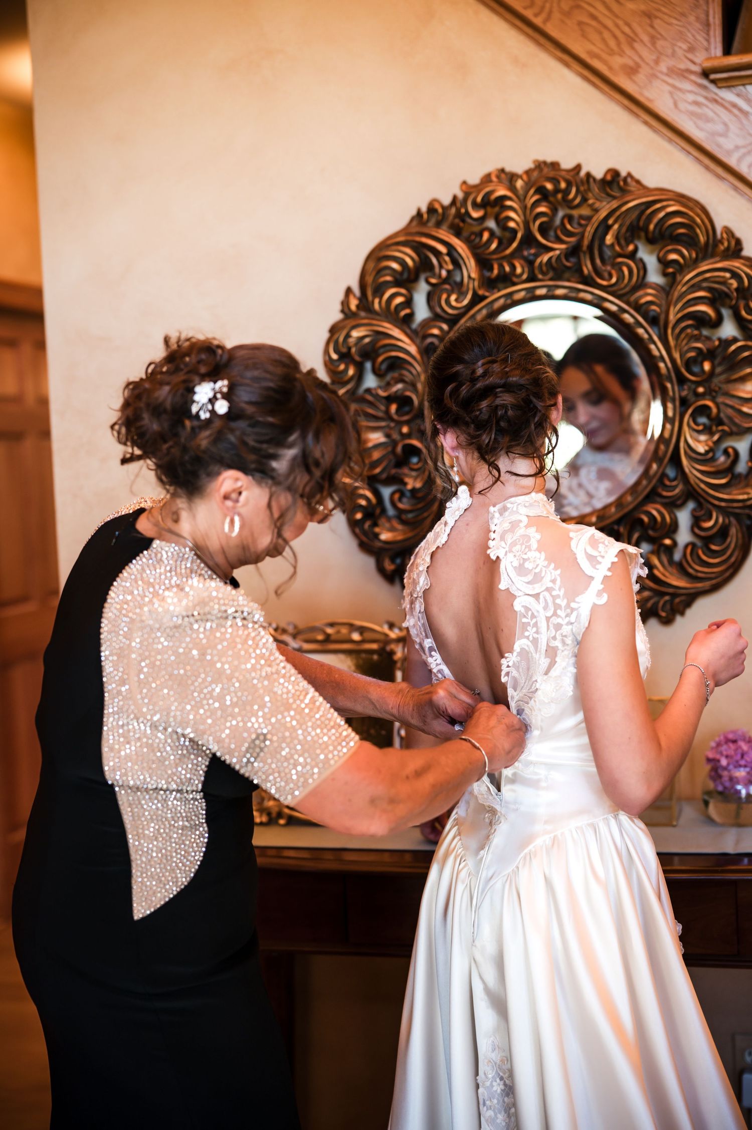 Two people share an emotional moment during a wedding ceremony in front of ornate wall mirrors.