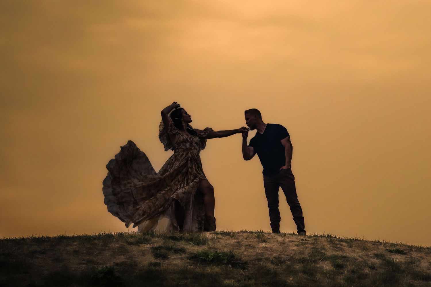 Silhouetted couple dancing on hilltop against dramatic sunset sky.