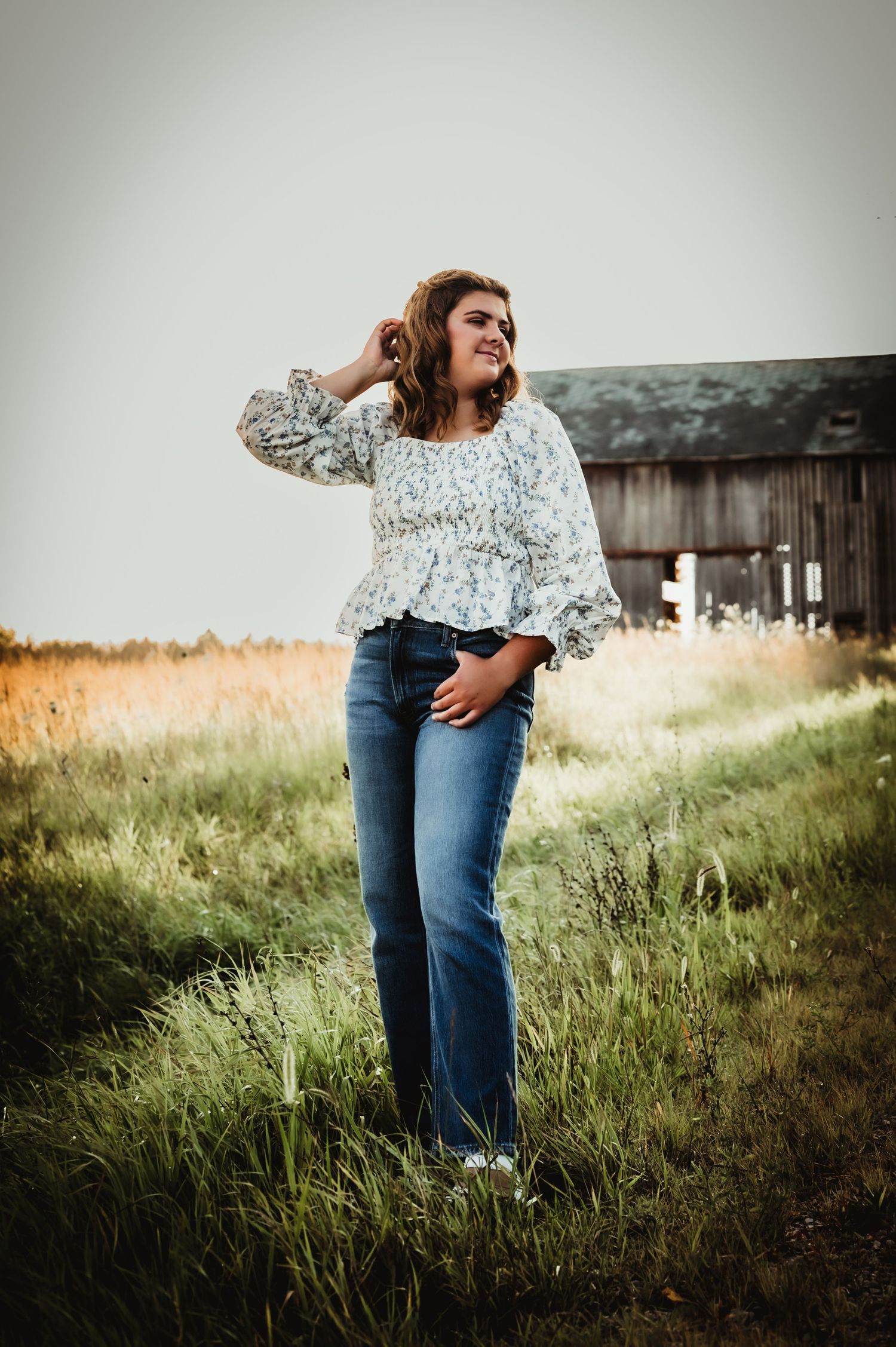 Casual outdoor portrait near weathered barn with tall grass in golden light.
