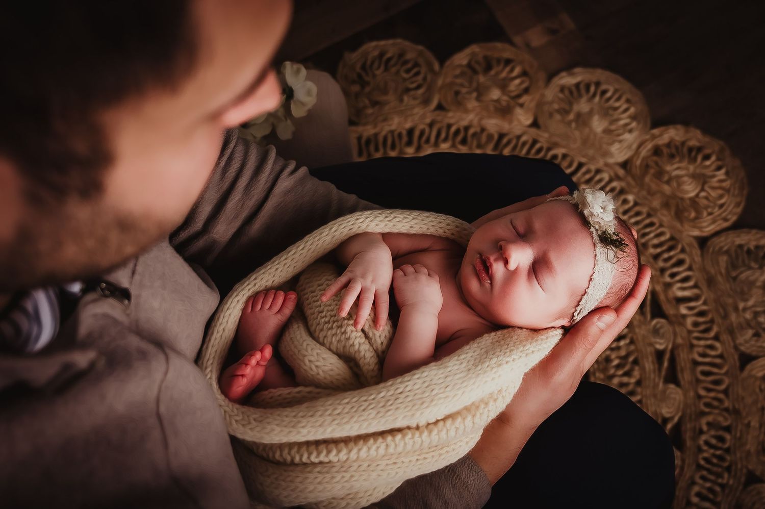 Sleeping newborn wrapped in knit blanket on vintage lace background.