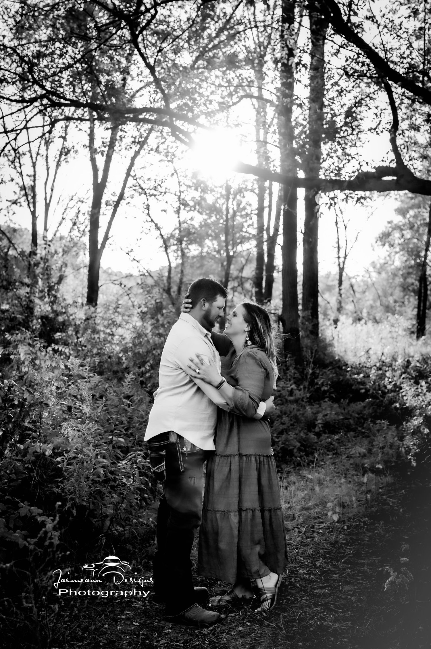 A black and white romantic moment captured between two people in a wooded forest setting.