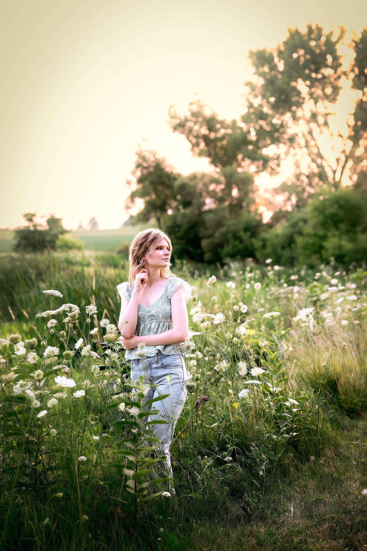 A person stands in a dreamy meadow of white wildflowers at sunset with soft golden light filtering through trees in Eden, WI