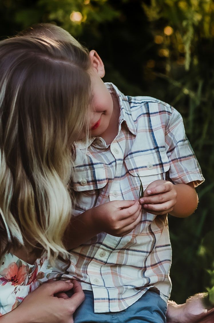 Candid moment of child examining something while sitting outdoors in checkered shirt.