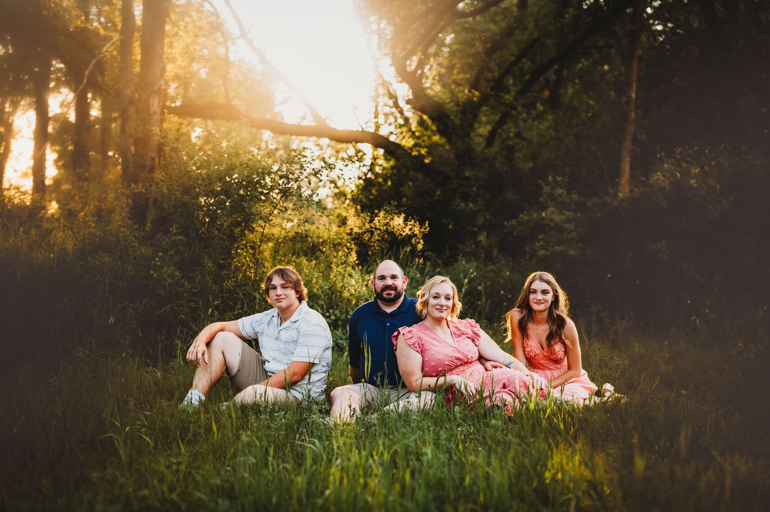 People sitting together in tall grass during sunset with trees in the background.
