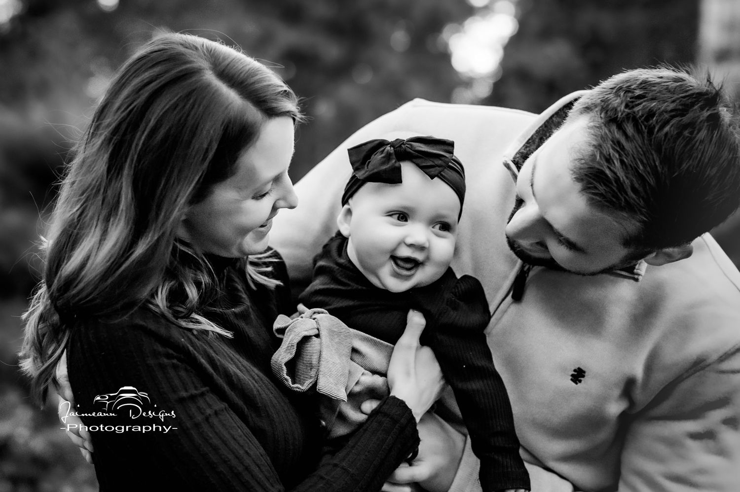 Black and white portrait of parents with baby sharing intimate moment outdoors.