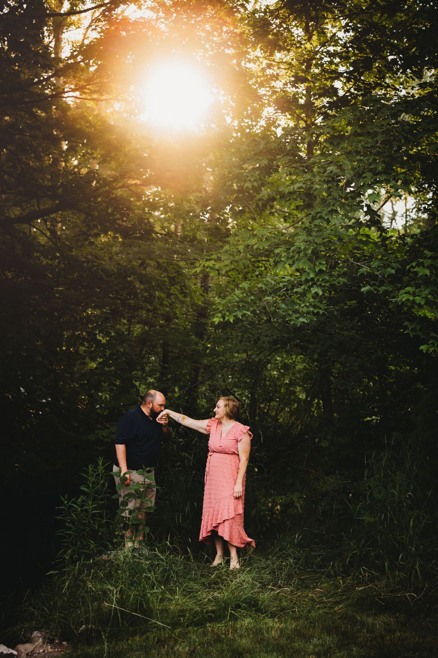 Couple shares romantic moment in sunlit forest clearing during golden hour.
