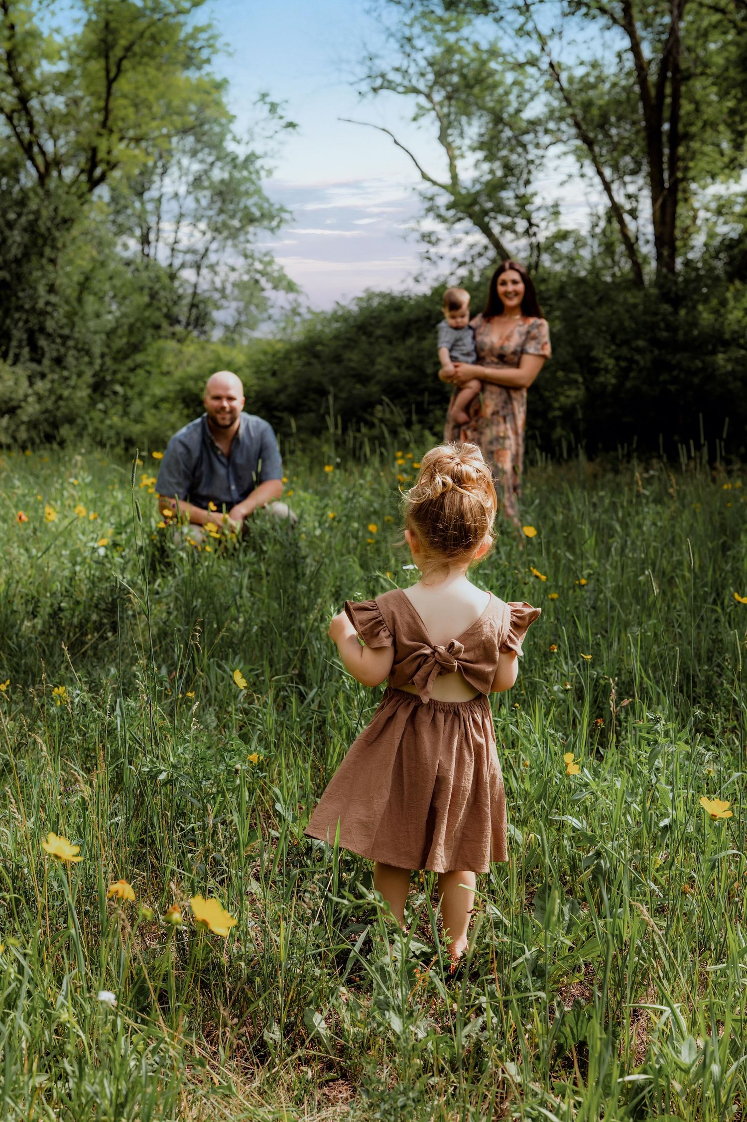 A young family enjoys a golden hour moment in a lush green meadow with wildflowers.