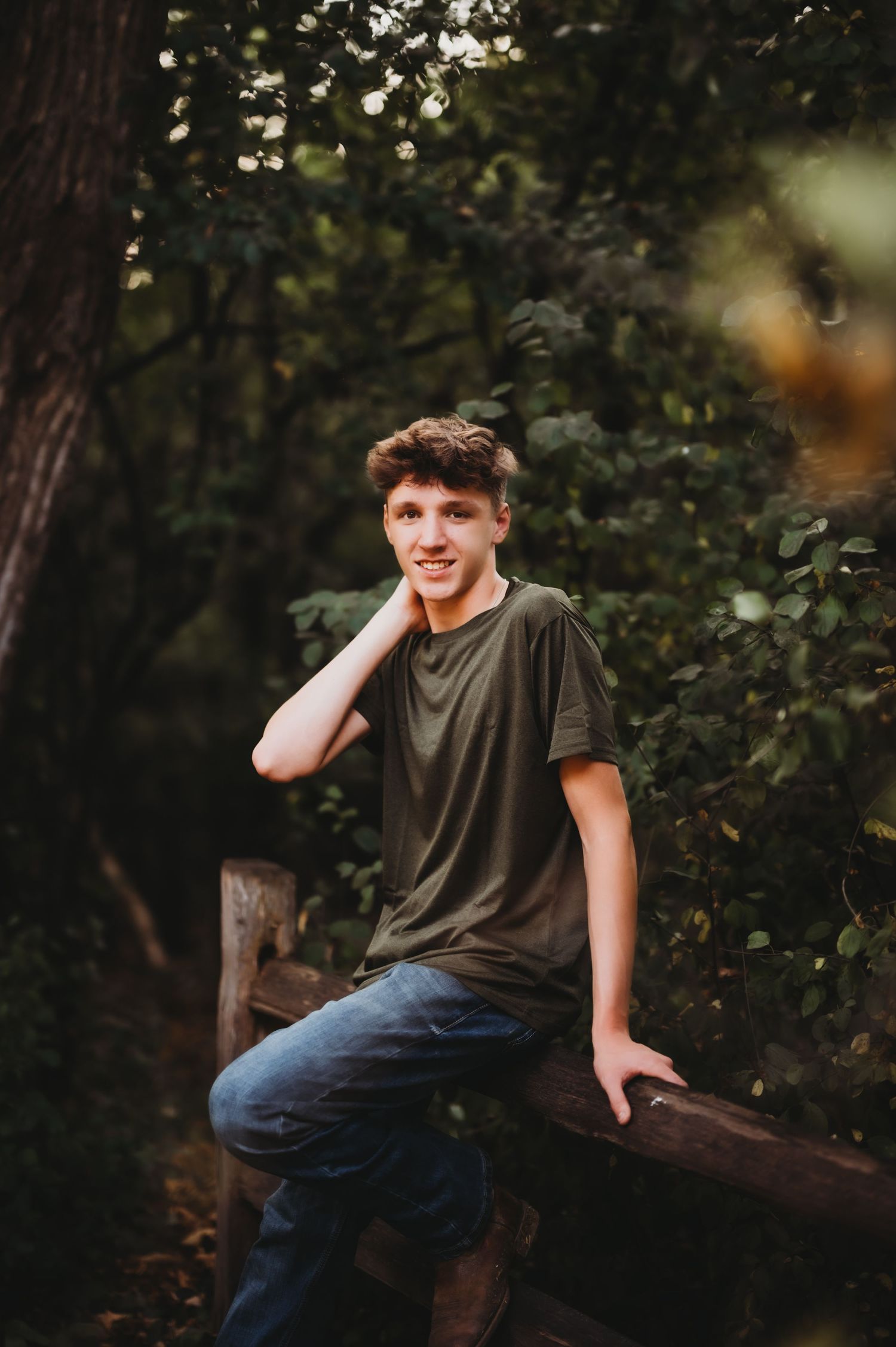 Person sitting on wooden fence in wooded area during golden hour.