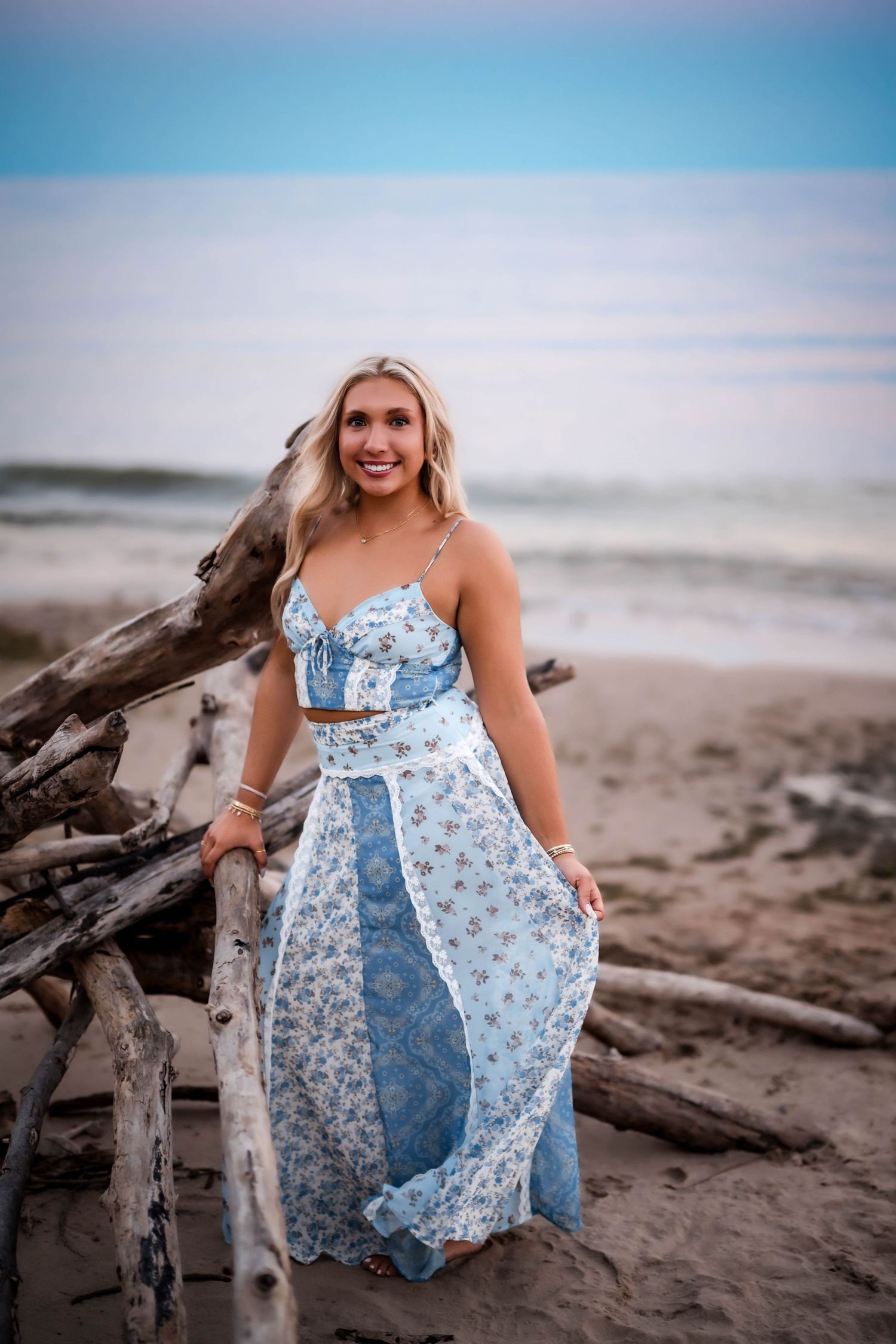 Senior girl holding her blue floral maxi dress on a Lake Michigan beach at sunset