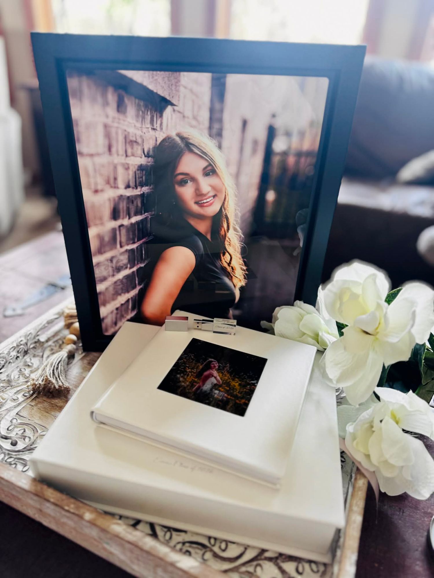Framed senior portrait photo of a young woman in black, displayed on a decorative tray with white roses and a photo box.