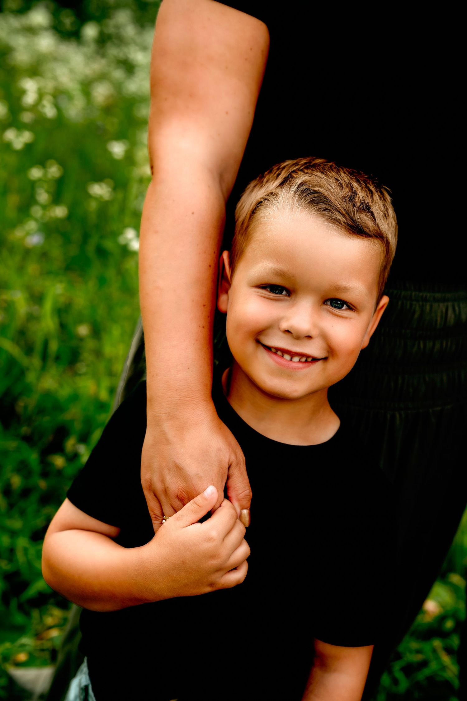 A child hugs an adult wearing black clothing while standing outdoors among greenery and flowers, Wisconsin