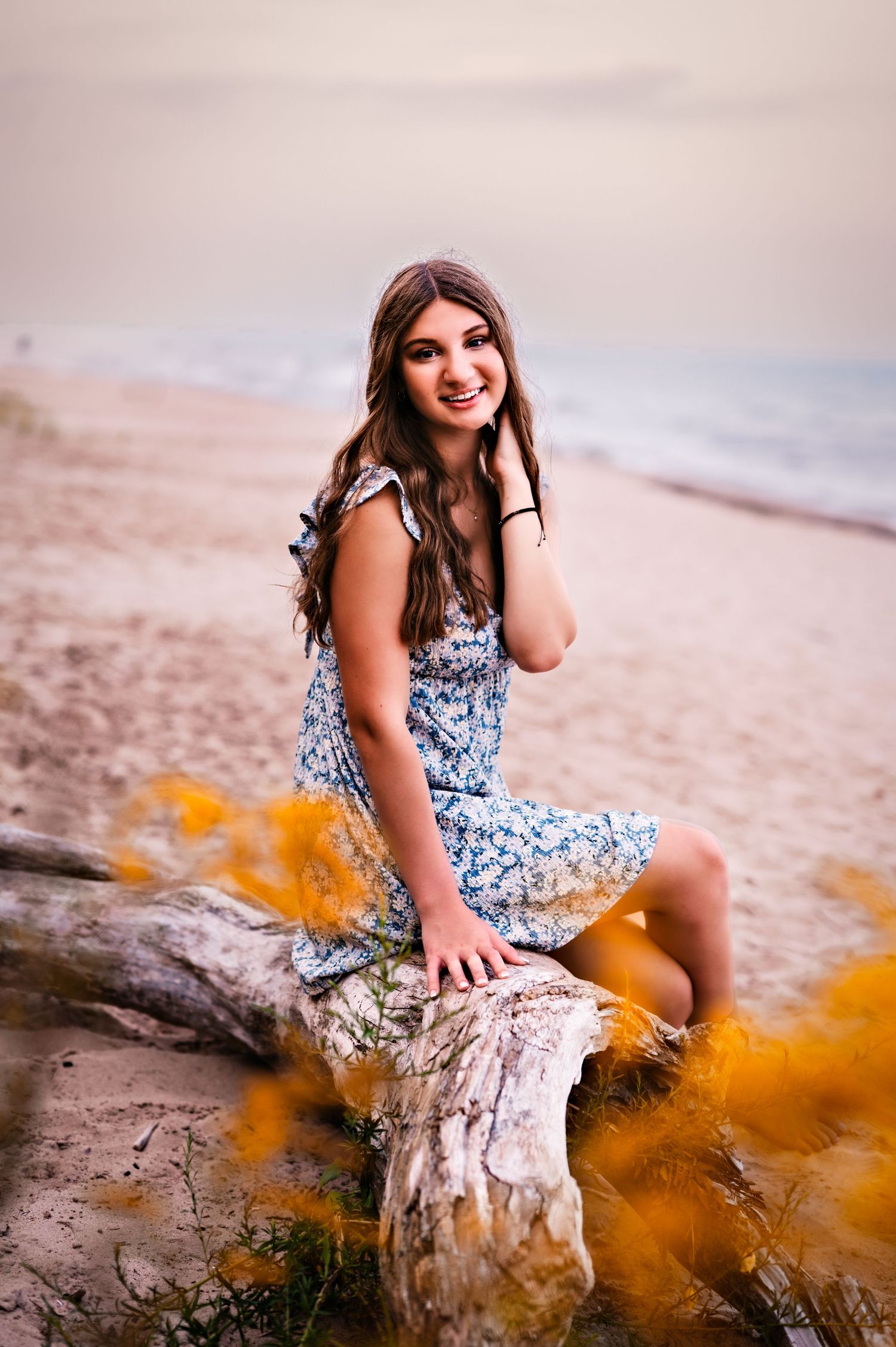 A person in a floral dress poses on a beach while orange smoke creates a dreamy atmosphere in a photo series on Beach in Sheboygan, WI
