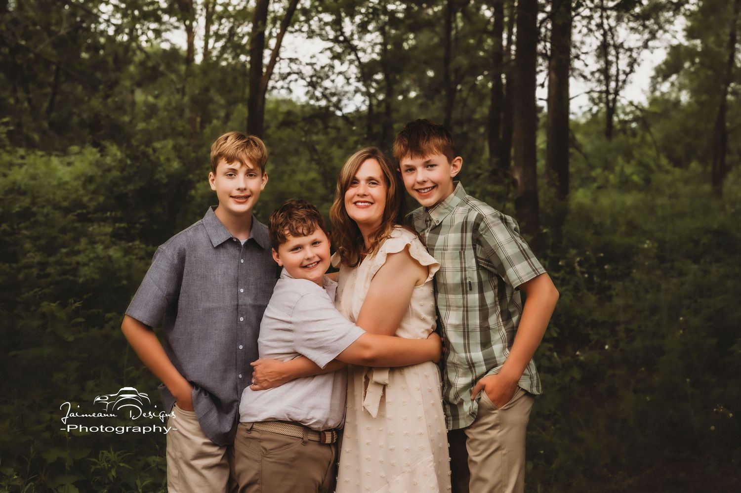 A family of four poses together in coordinated outfits against a forested backdrop.