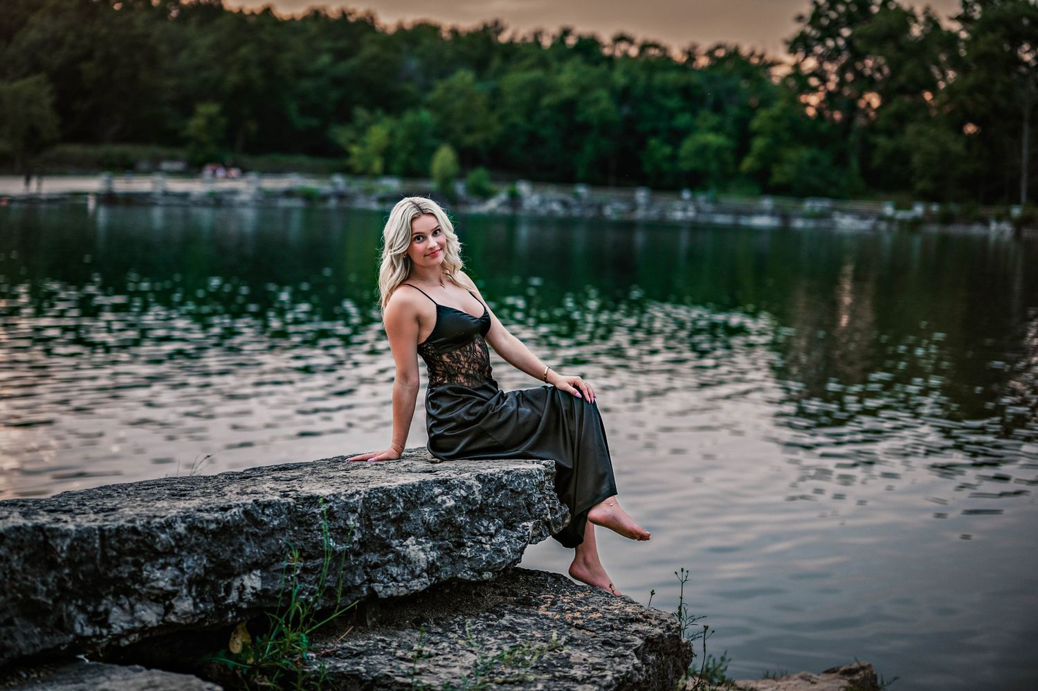 A person in a black dress poses gracefully by a serene lake at sunset creating artistic silhouettes on the water. Senior Photos, WI