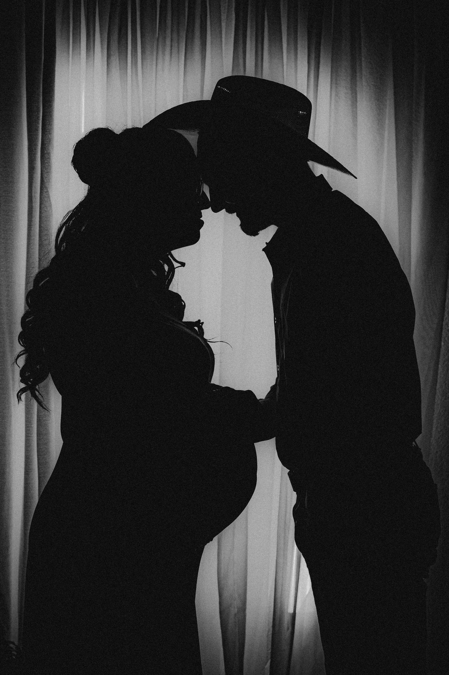 Silhouette portrait of a couple with a cowboy hat in an intimate pose against a light backdrop.