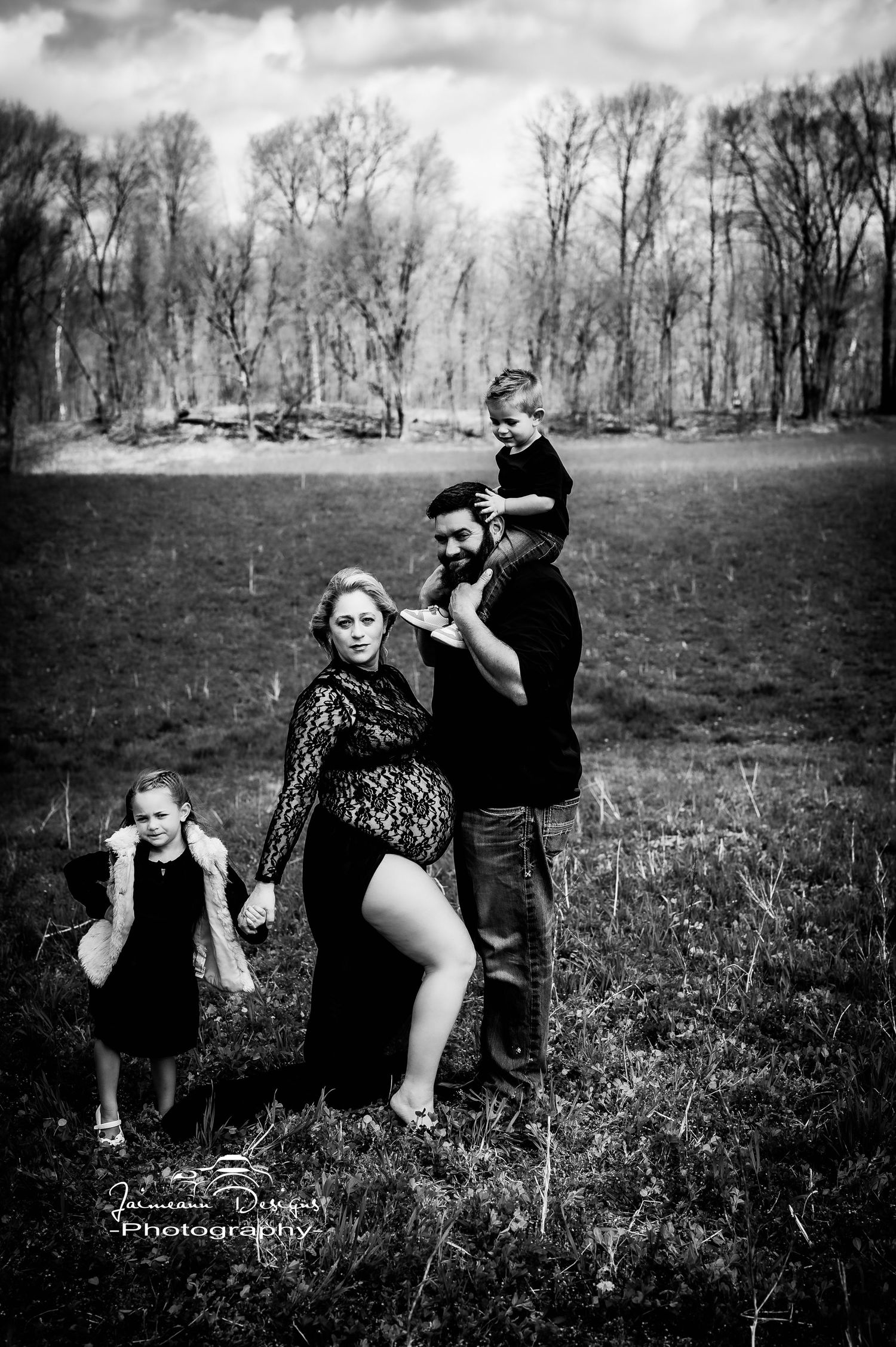 Black and white family portrait with playful poses in natural setting.