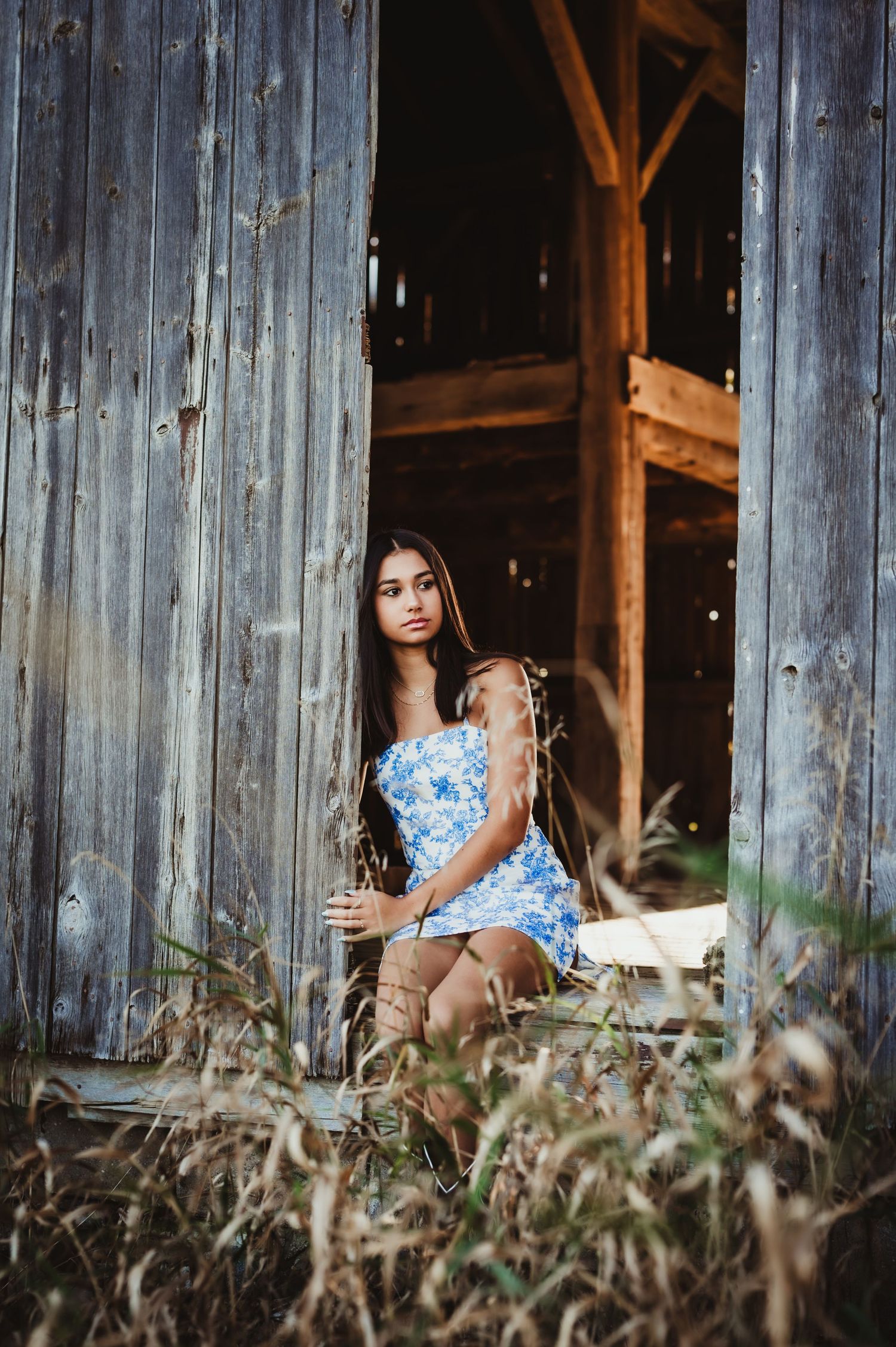 Fashion portrait at old barn entrance with wildflowers and wooden backdrop.