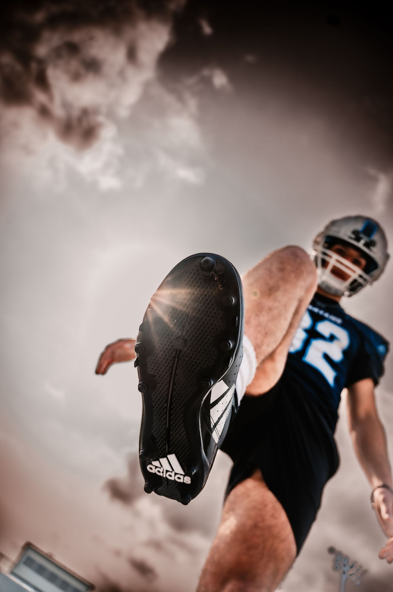 Low angle action shot of a football player kicking with an Adidas cleat against dramatic cloudy sky, WEst Bend High School,  WI