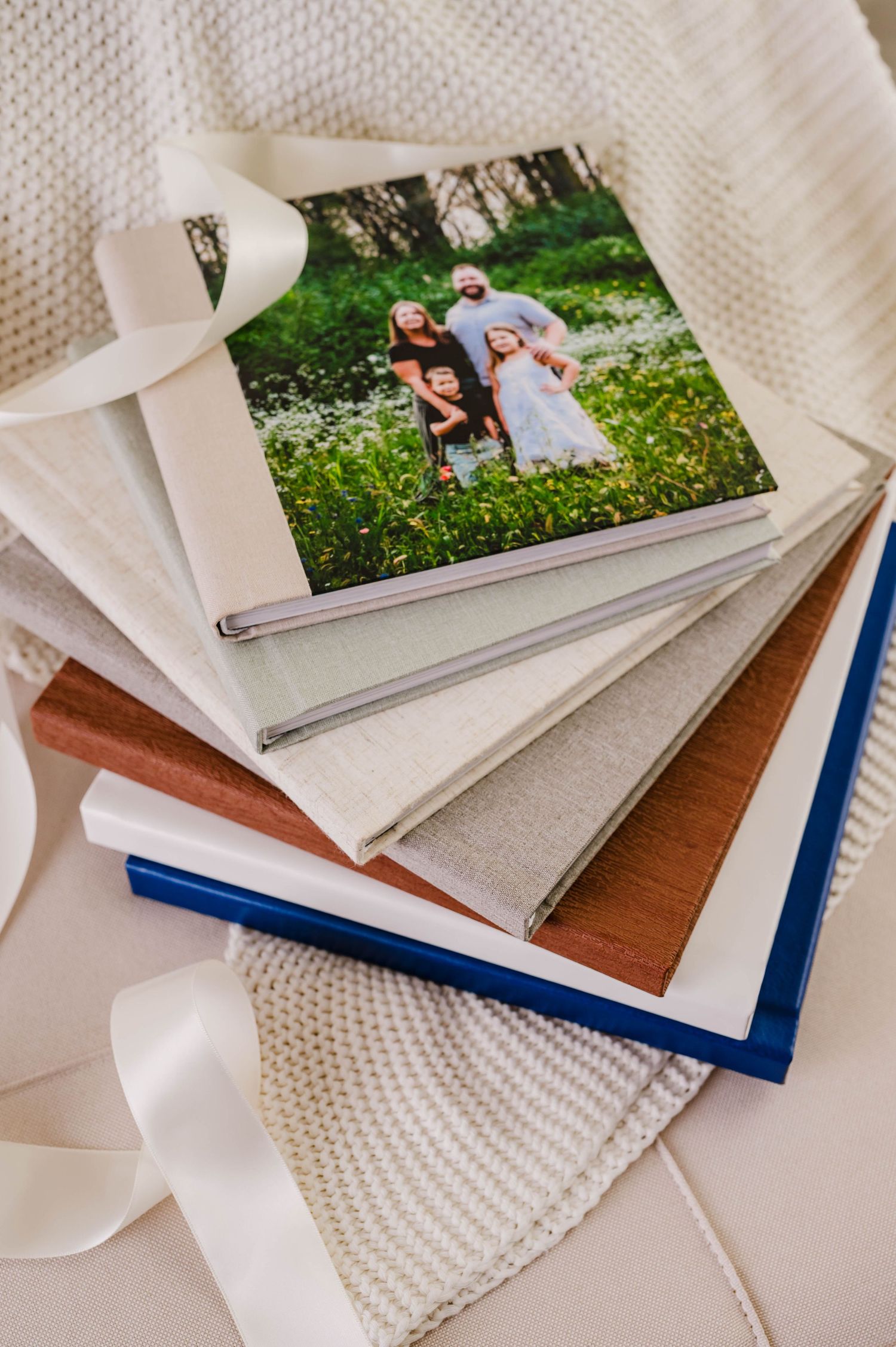 Stack of family photo albums with ribbon, featuring a family portrait cover photo in a lush green outdoor setting.