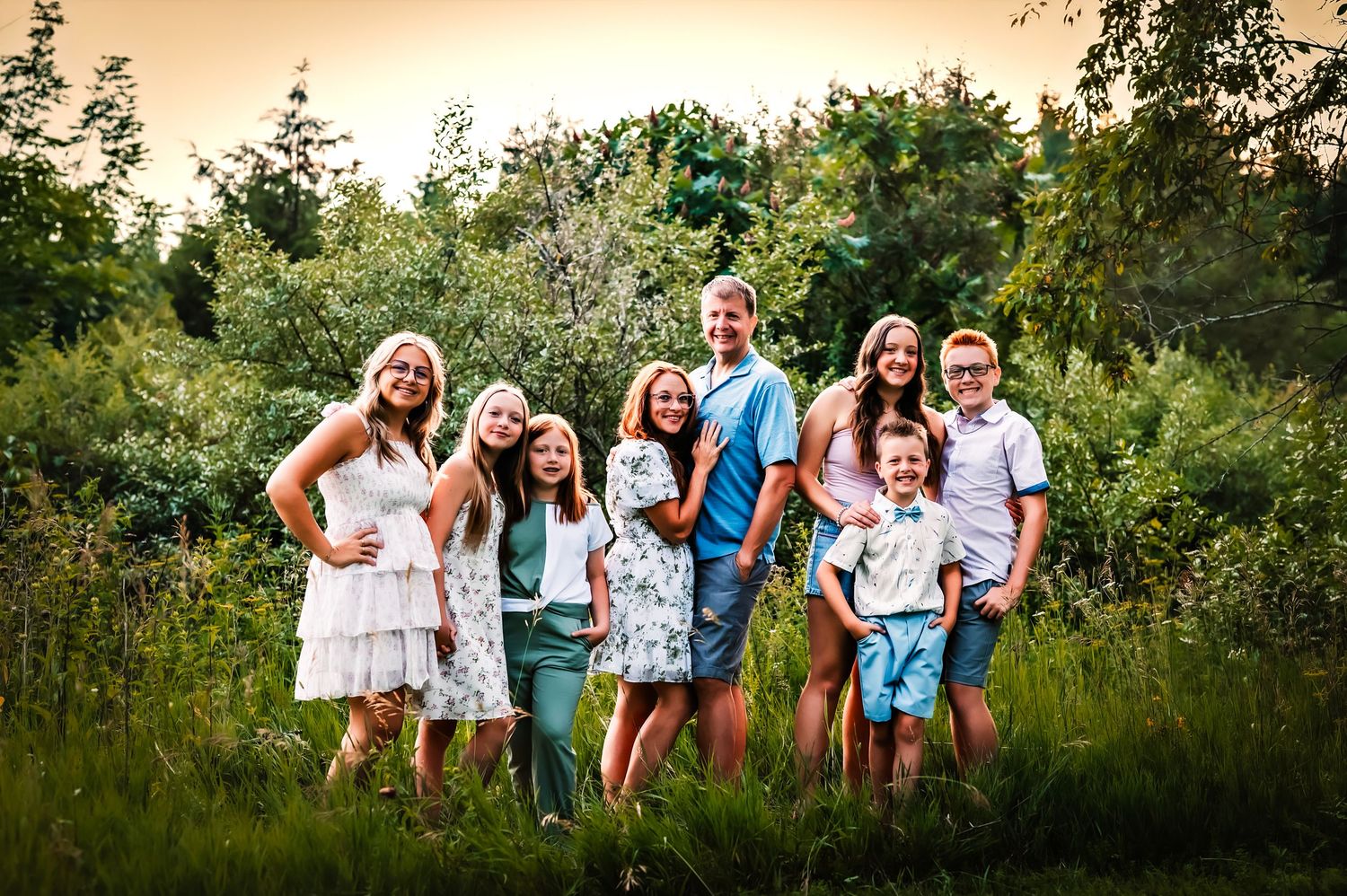 A group in coordinated white and blue outfits walks through a lush green field at sunset, Big Cedar Lake, WI