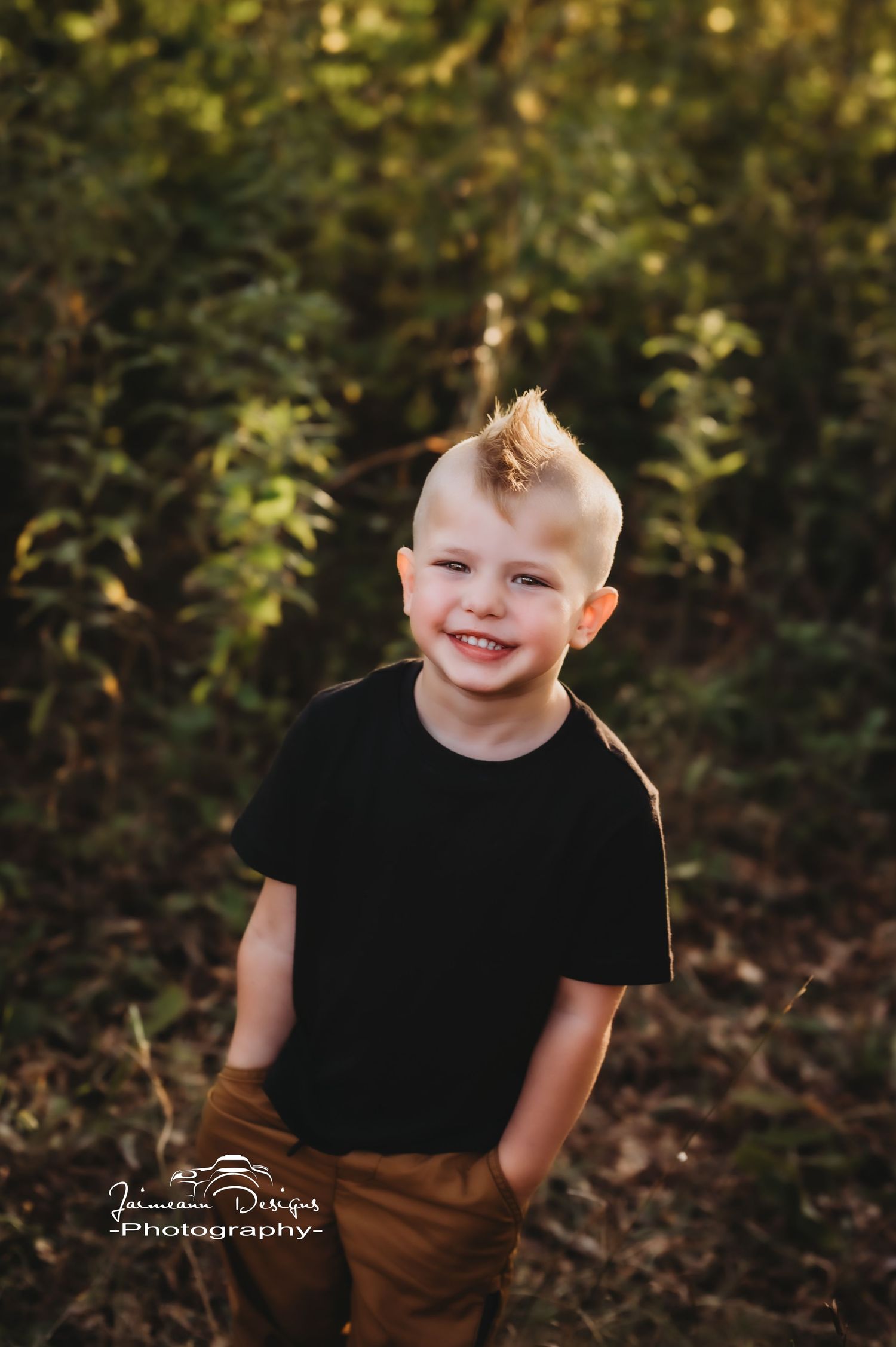 A young child wearing a black t-shirt smiles outdoors with a stylish mohawk hairstyle.