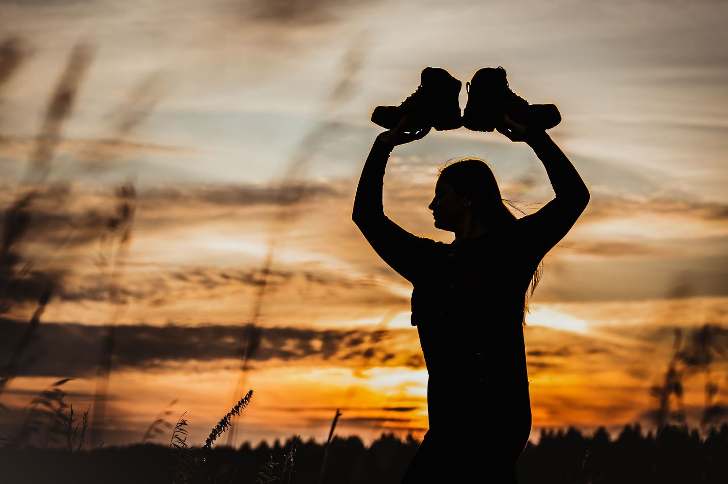 Silhouette of person holding boots against dramatic sunset sky.