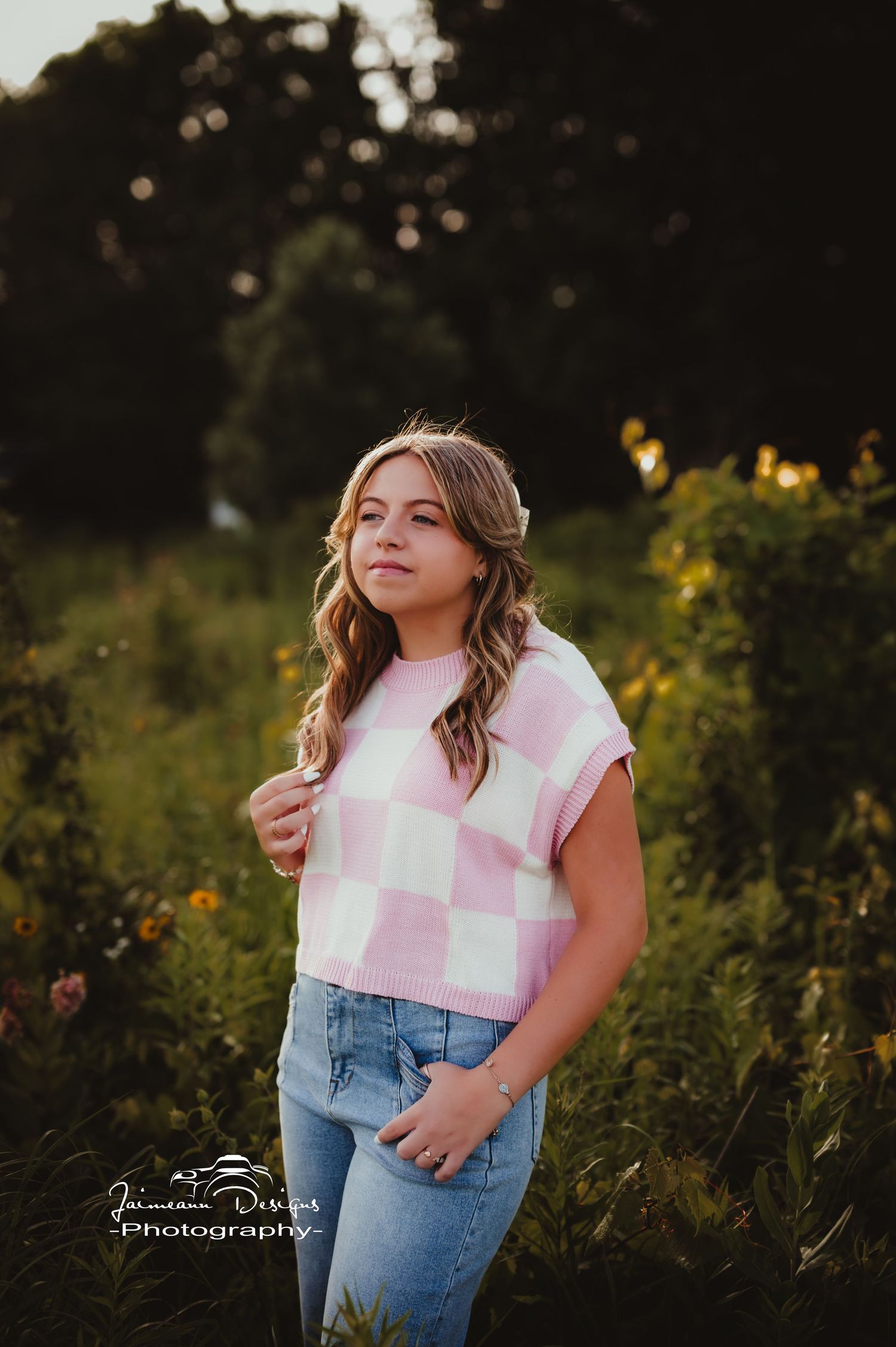 Portrait in pink checkered shirt and jeans with natural sunset lighting and greenery.