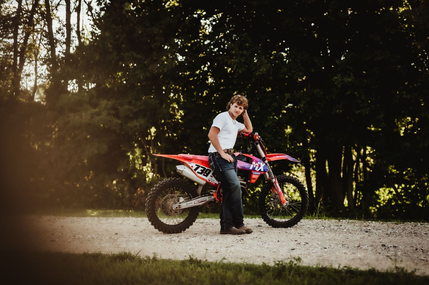 Outdoor portrait with dirt bike and rider at sunset in a wooded area.