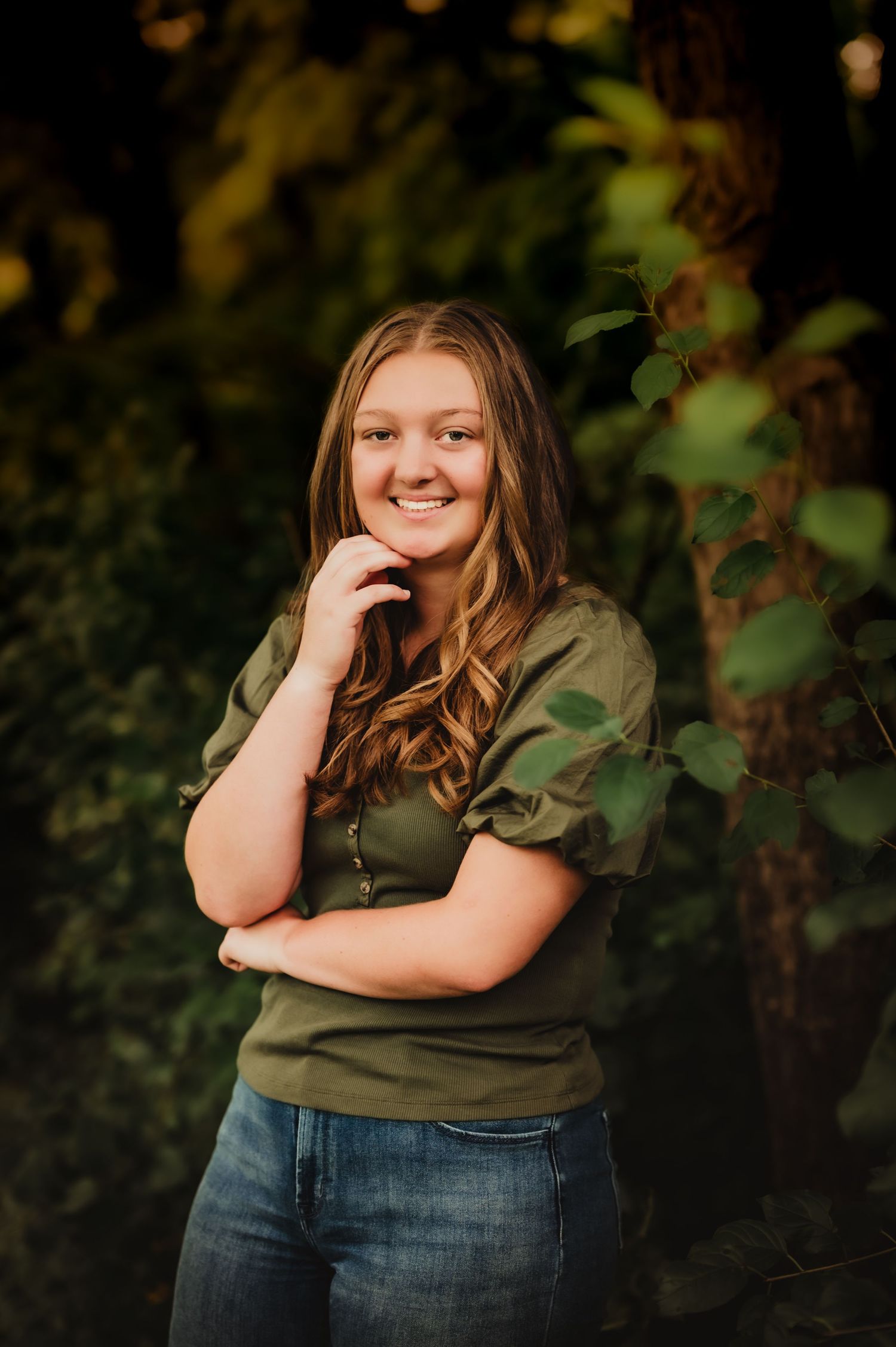 Natural portrait in green top and jeans against leafy garden background.