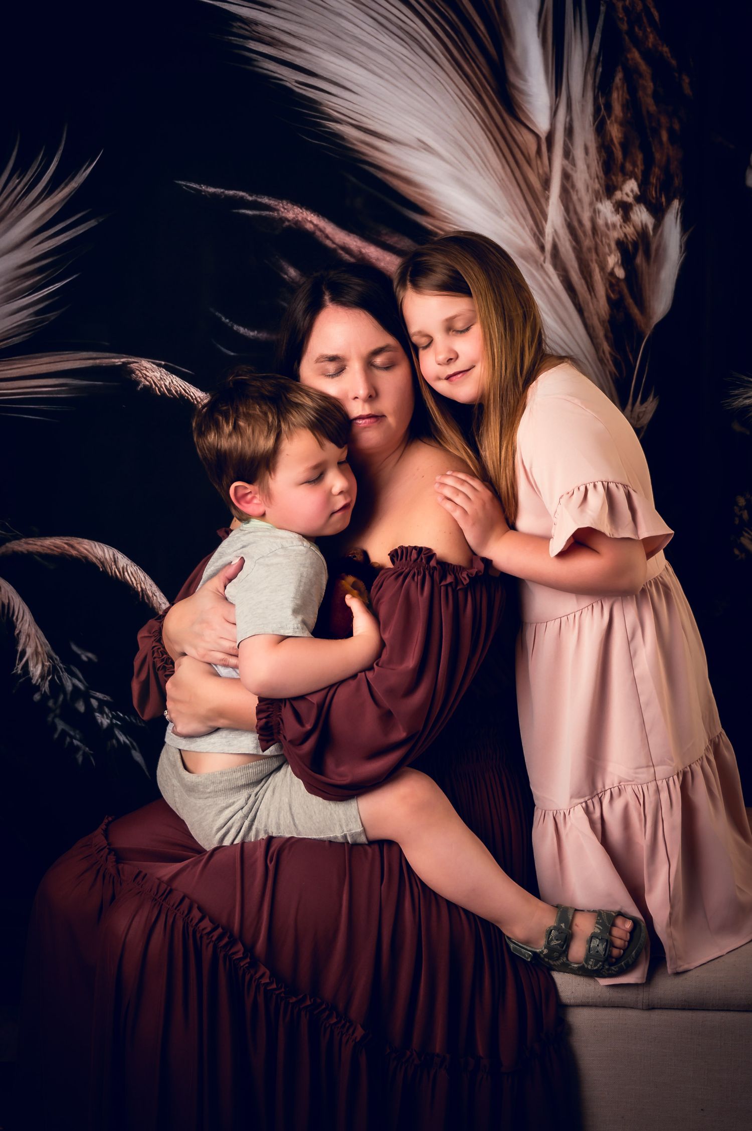 Intimate family portrait with burgundy dress against dark backdrop with white feathers.