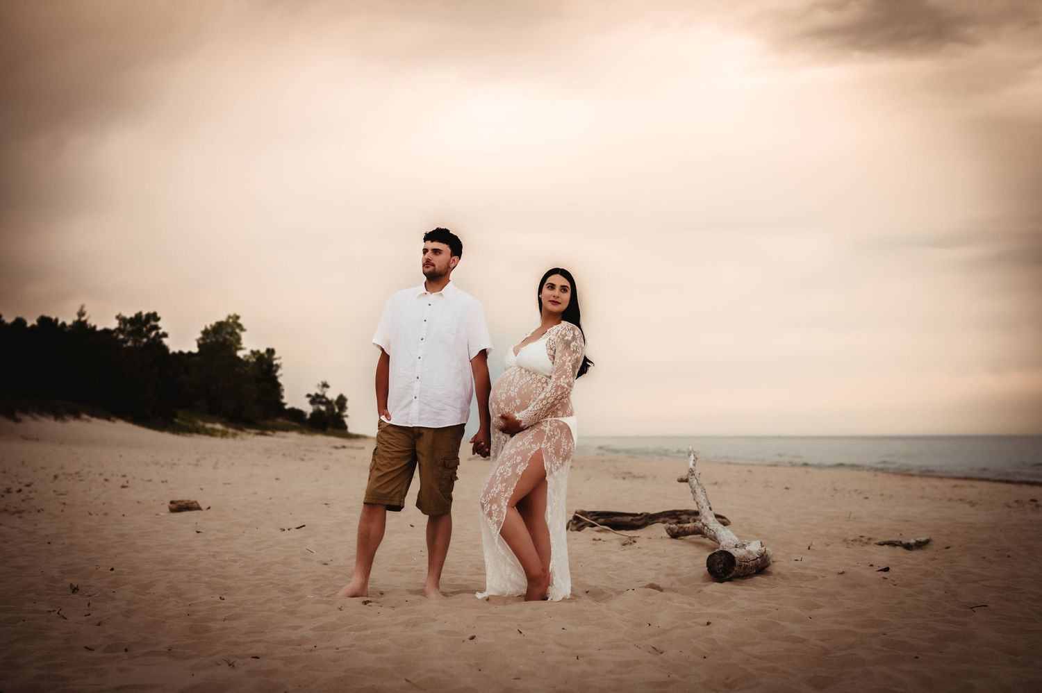 Couple standing together on beach at sunset with dramatic sky.
