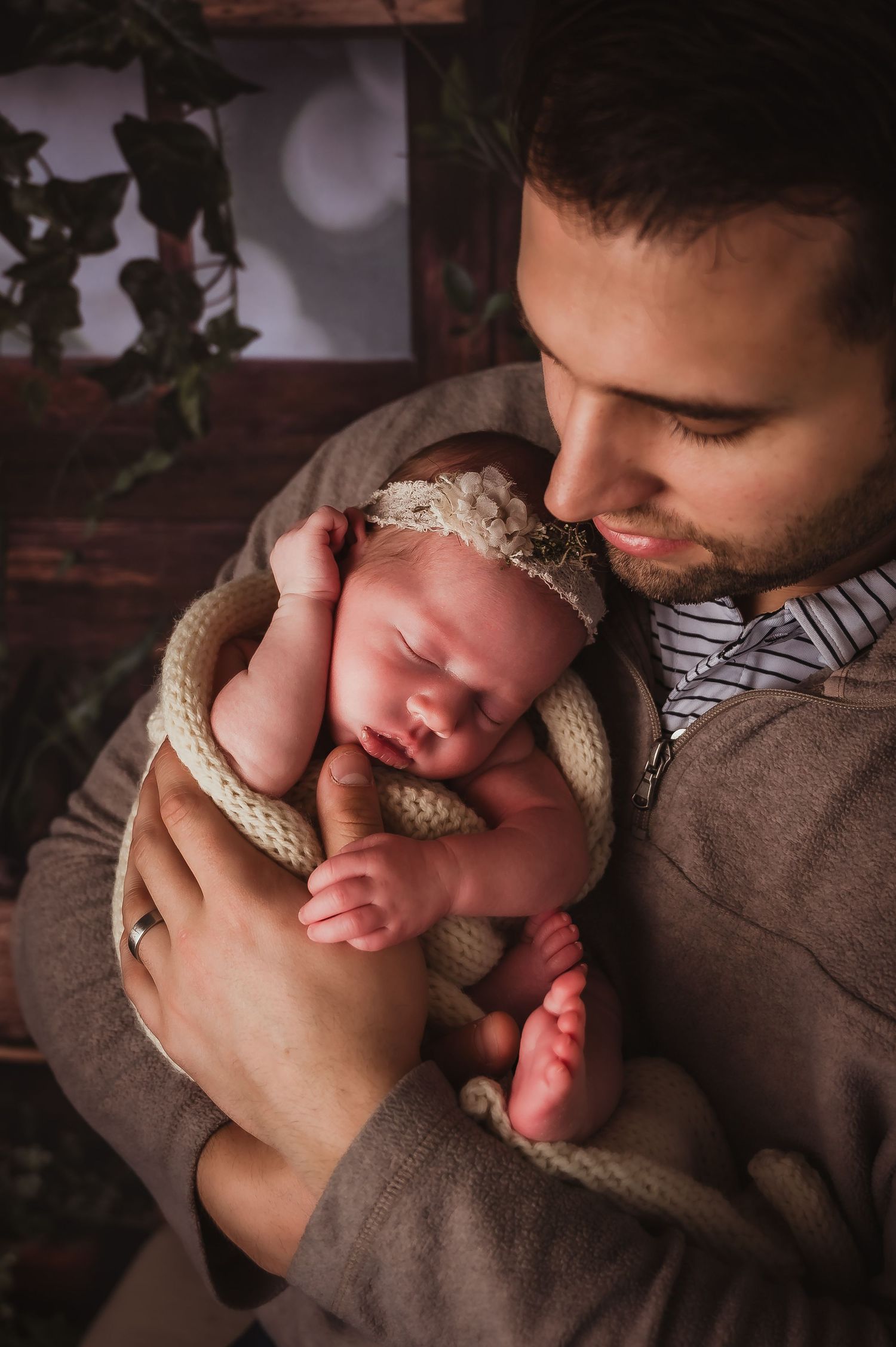 Tender moment between parent and sleeping newborn wrapped in cream knit blanket.