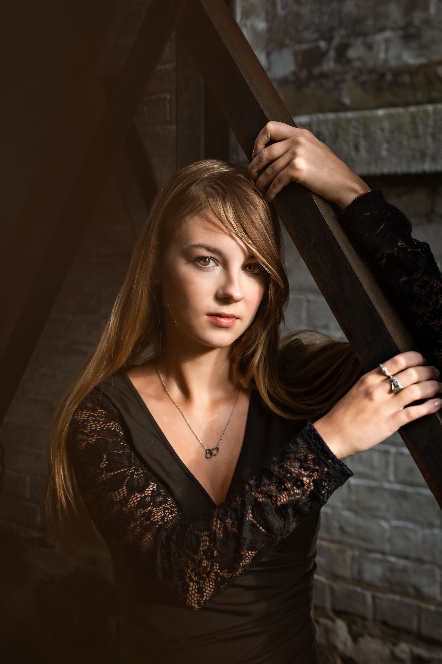 Portrait of someone wearing a black lace v-neck top posing against a dark wall with dramatic lighting in Cedarburg, WI