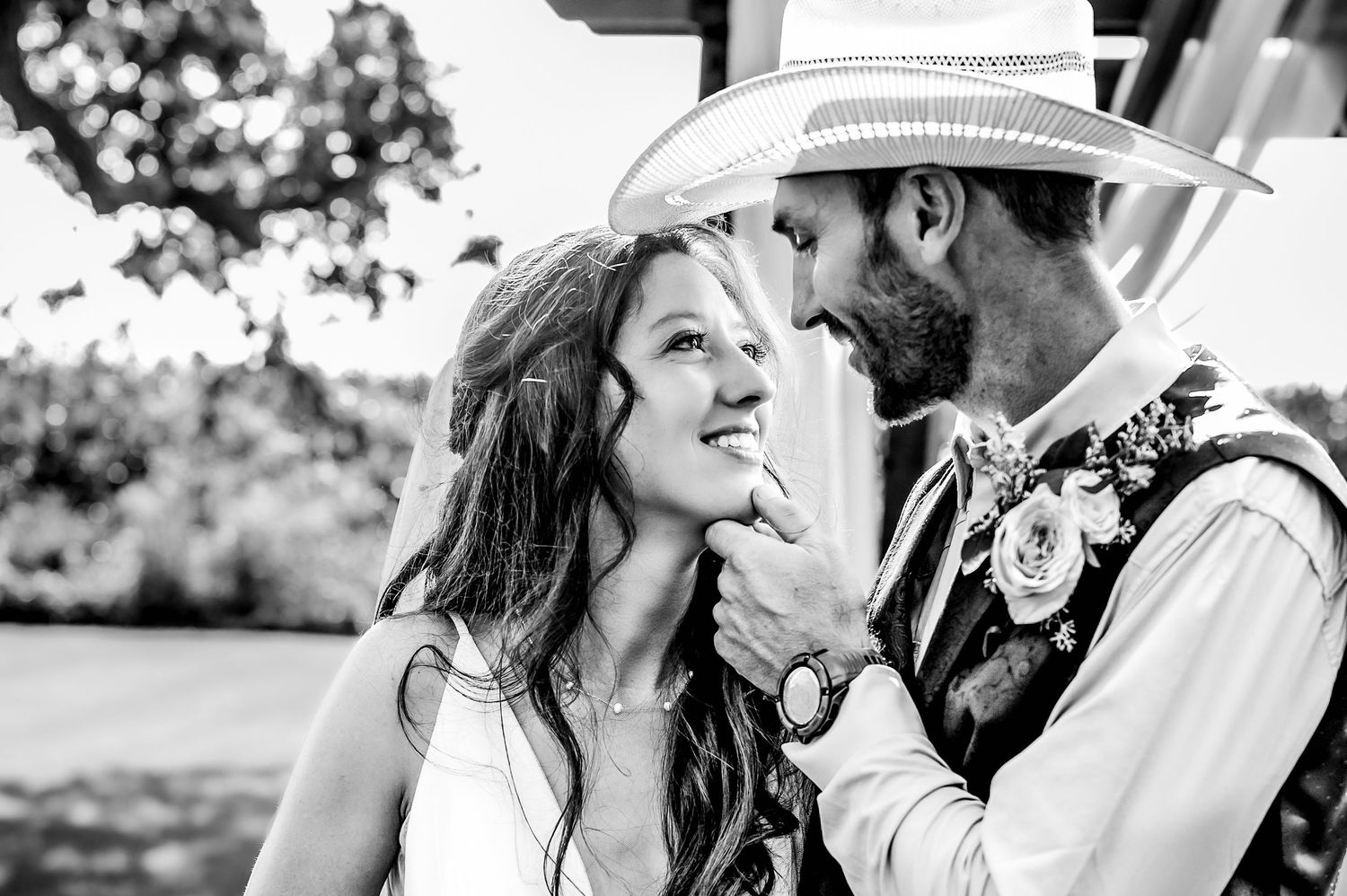 A couple in wedding attire shares an intimate moment together in a black and white outdoor portrait.