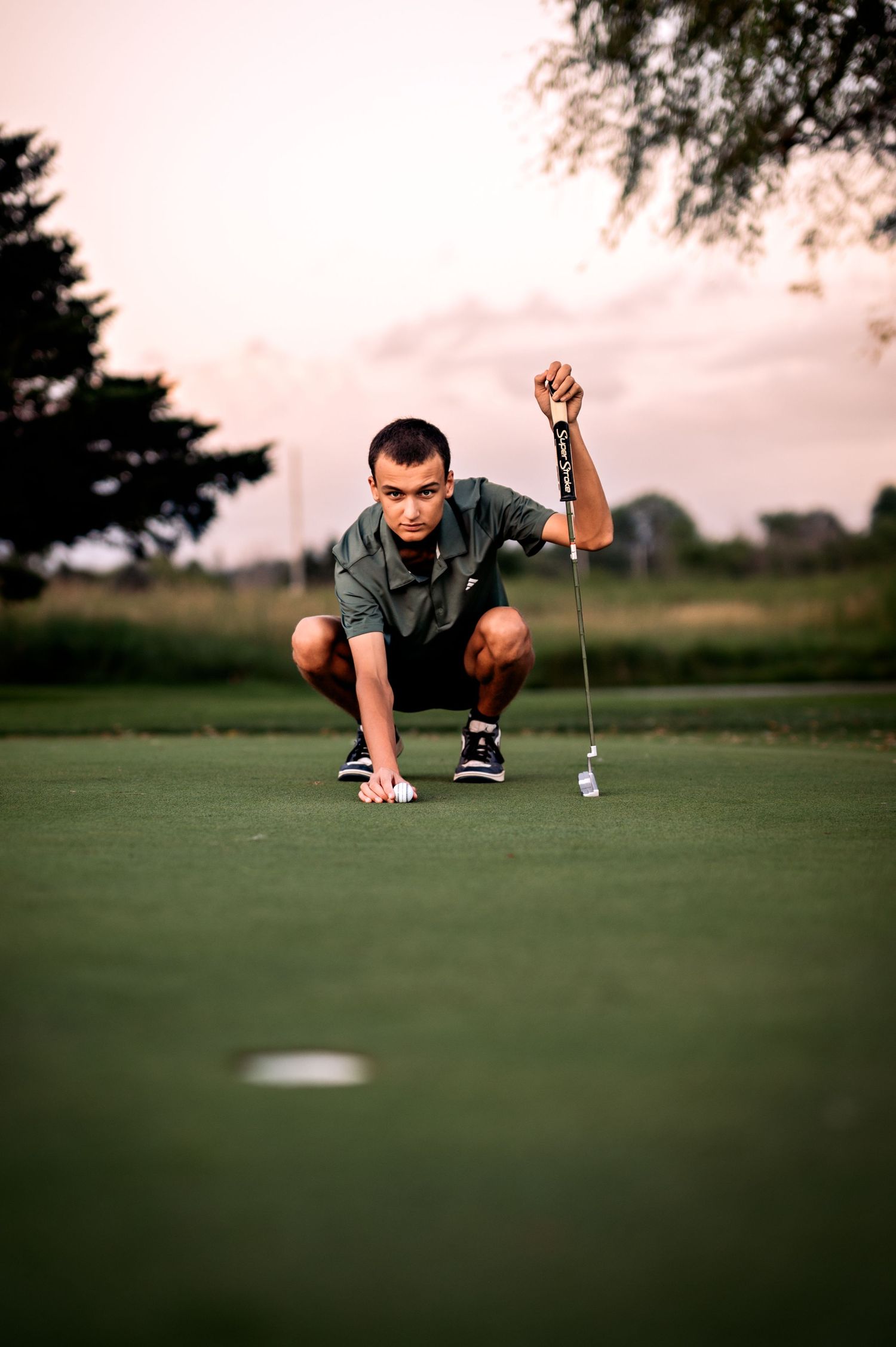 A golfer in a gray shirt lies on the green to analyze the putting line during a game of golf at Hon-e-kor Golf Course, WI