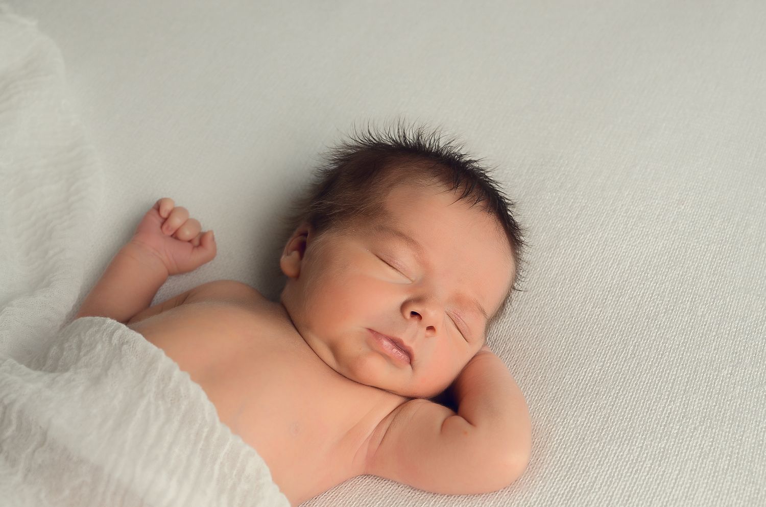 A sleeping newborn baby lies peacefully on soft white bedding in a series of connected photos.