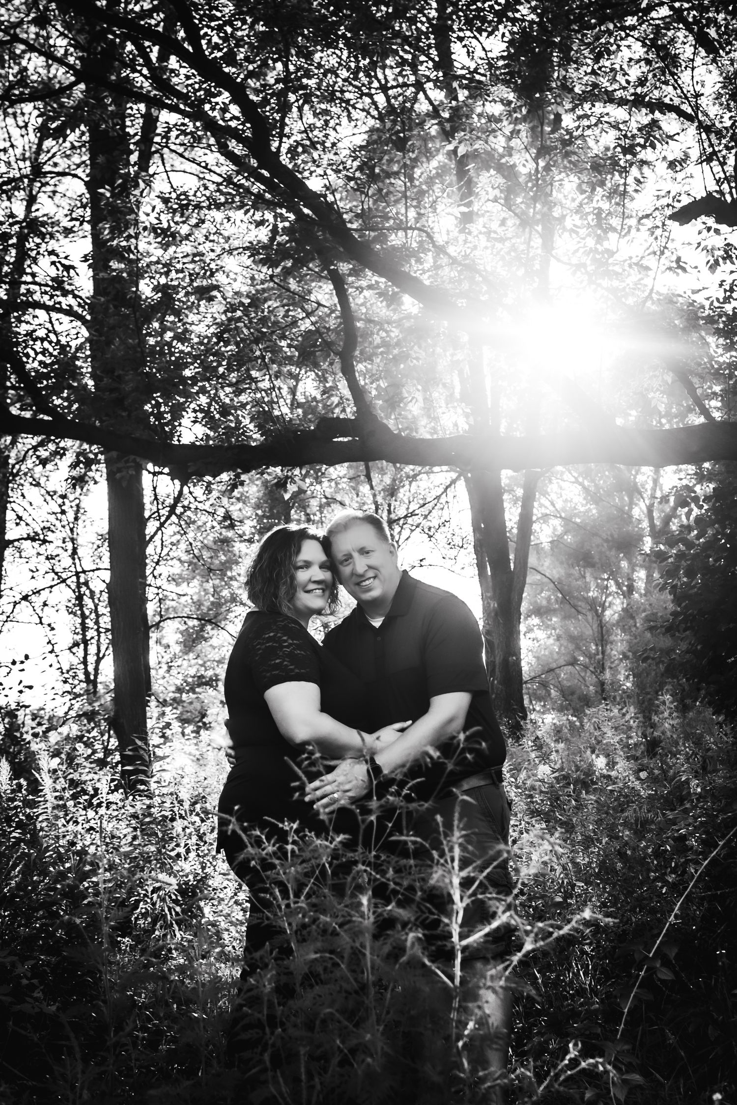 A couple embraces in a sunlit forest with dramatic backlighting creating a dreamy atmosphere.