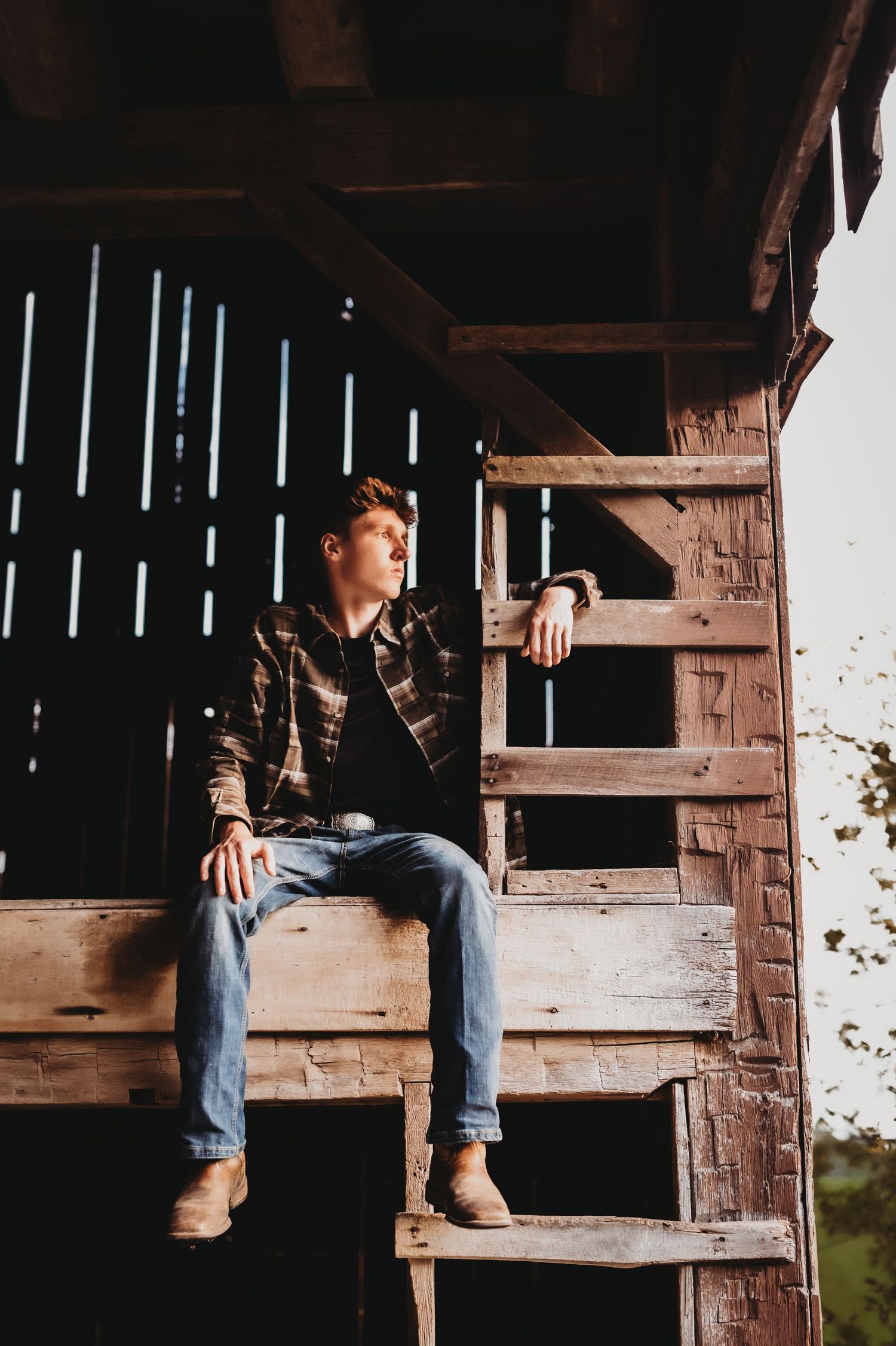 Person sitting on wooden steps inside rustic barn with slanted light coming through slats.