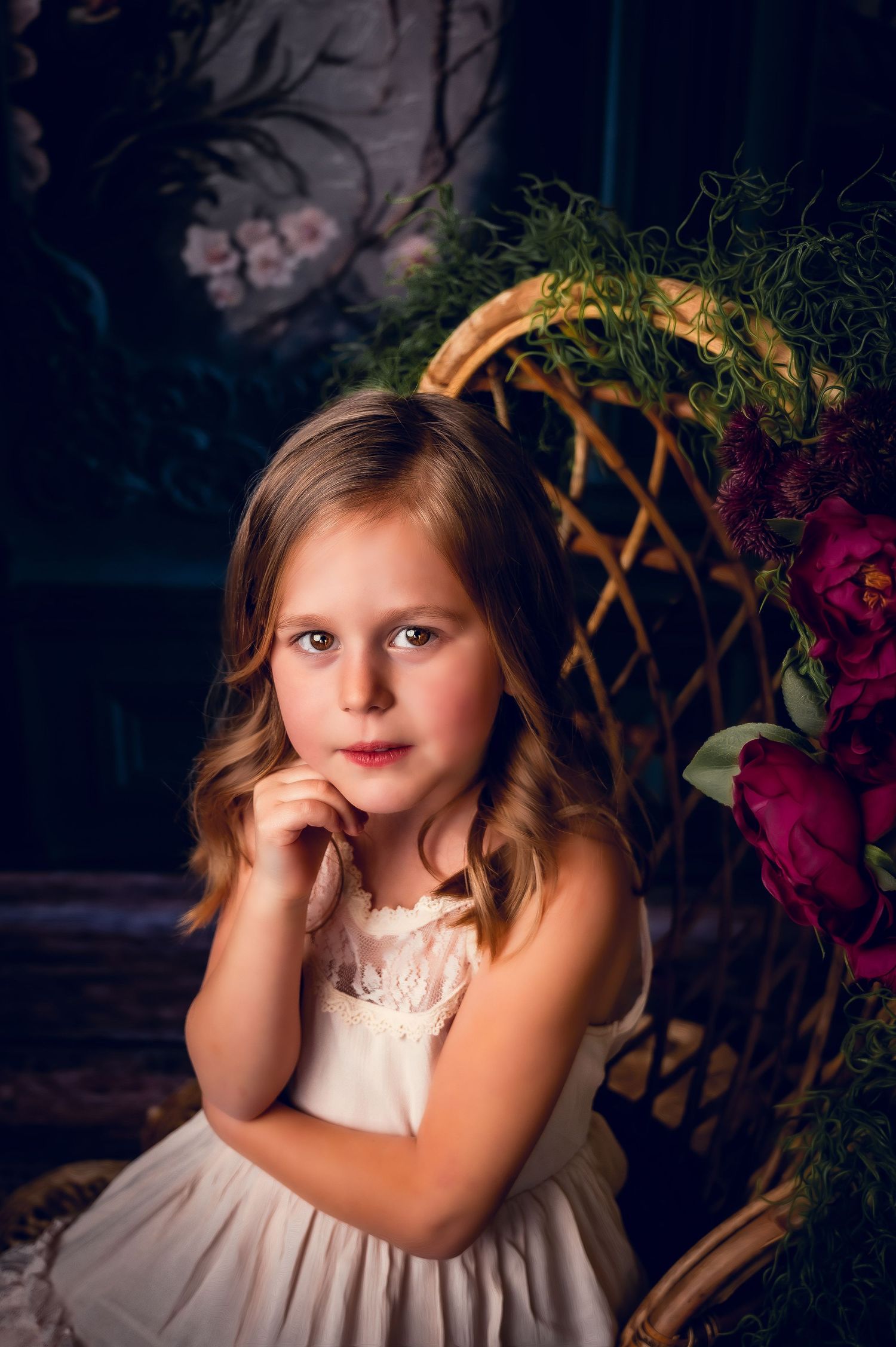 Portrait by vintage wicker chair with floral decorations in moody lighting.