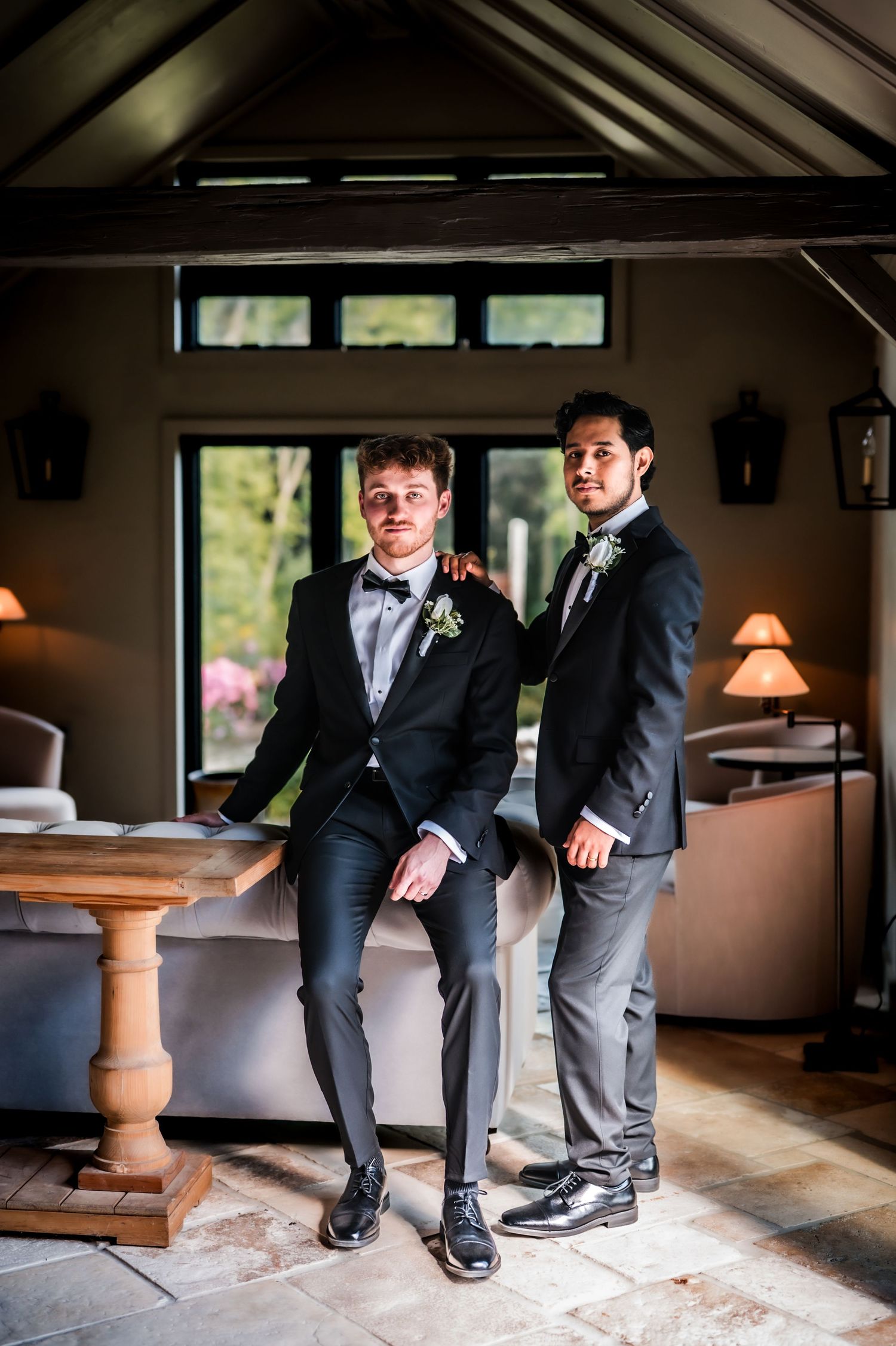 Groomsmen in formal attire posing casually in rustic indoor setting.