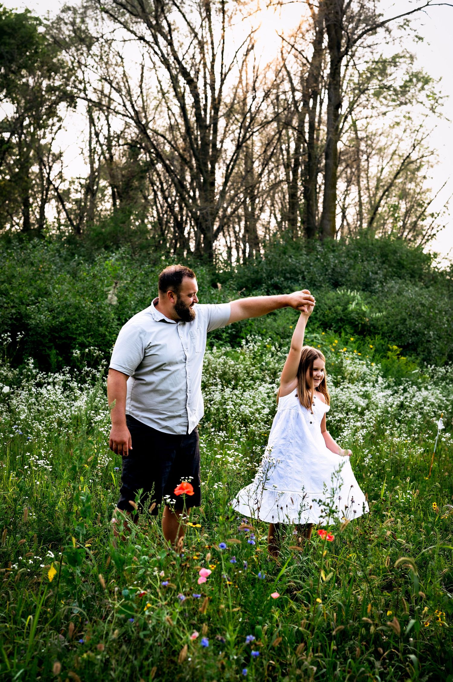 A parent and child dance together in a wildflower meadow at sunset among tall trees and blooming flowers. Fond du lac, WI