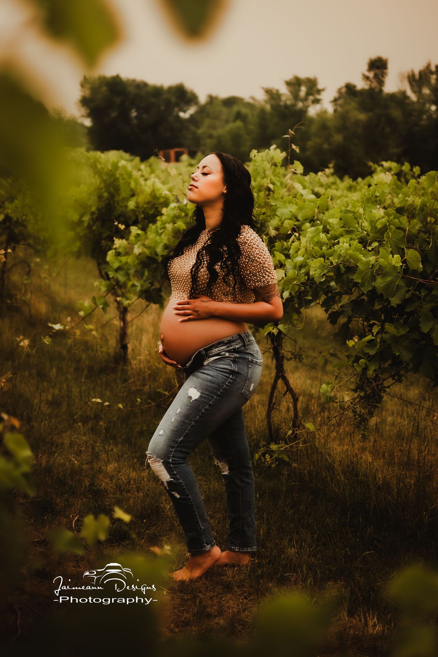 Artistic maternity portrait in a vineyard with warm lighting and natural greenery surroundings.