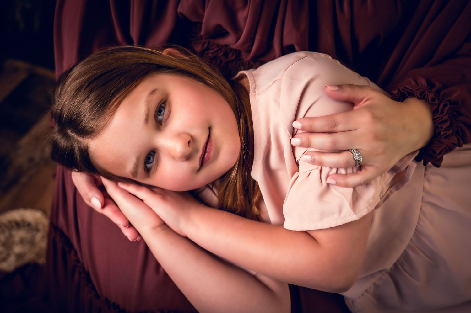 Portrait featuring soft pink dress against burgundy background in dreamy lighting.