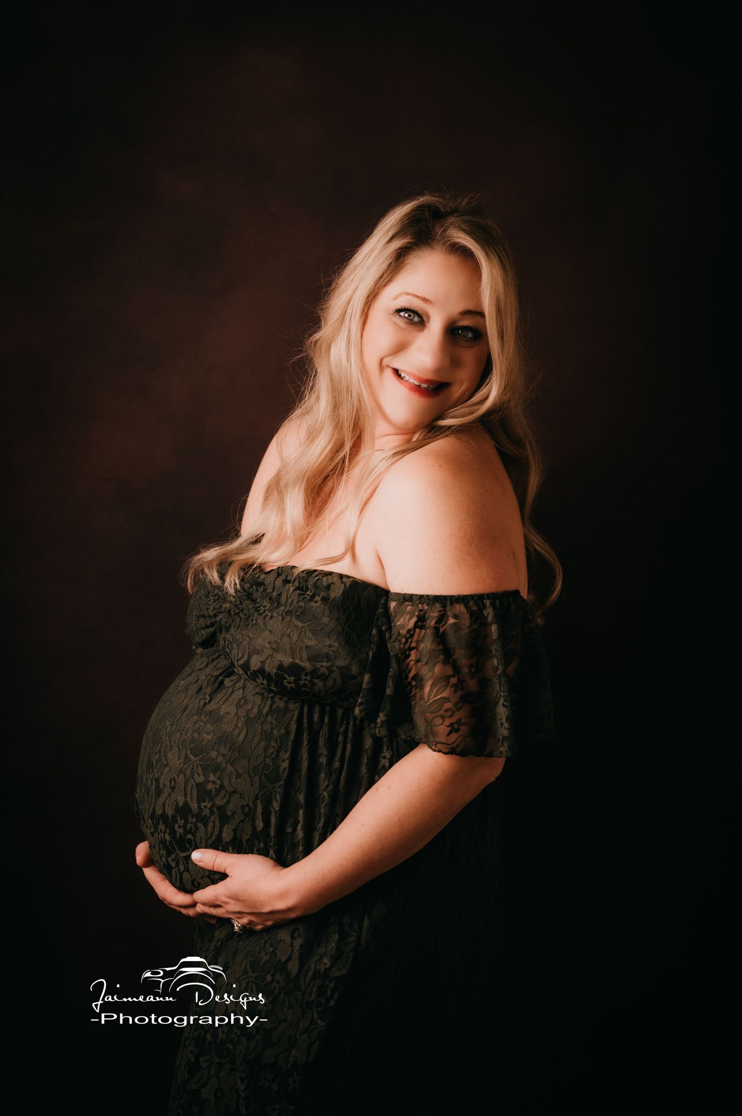 Classic maternity portrait in black lace dress against dark background.