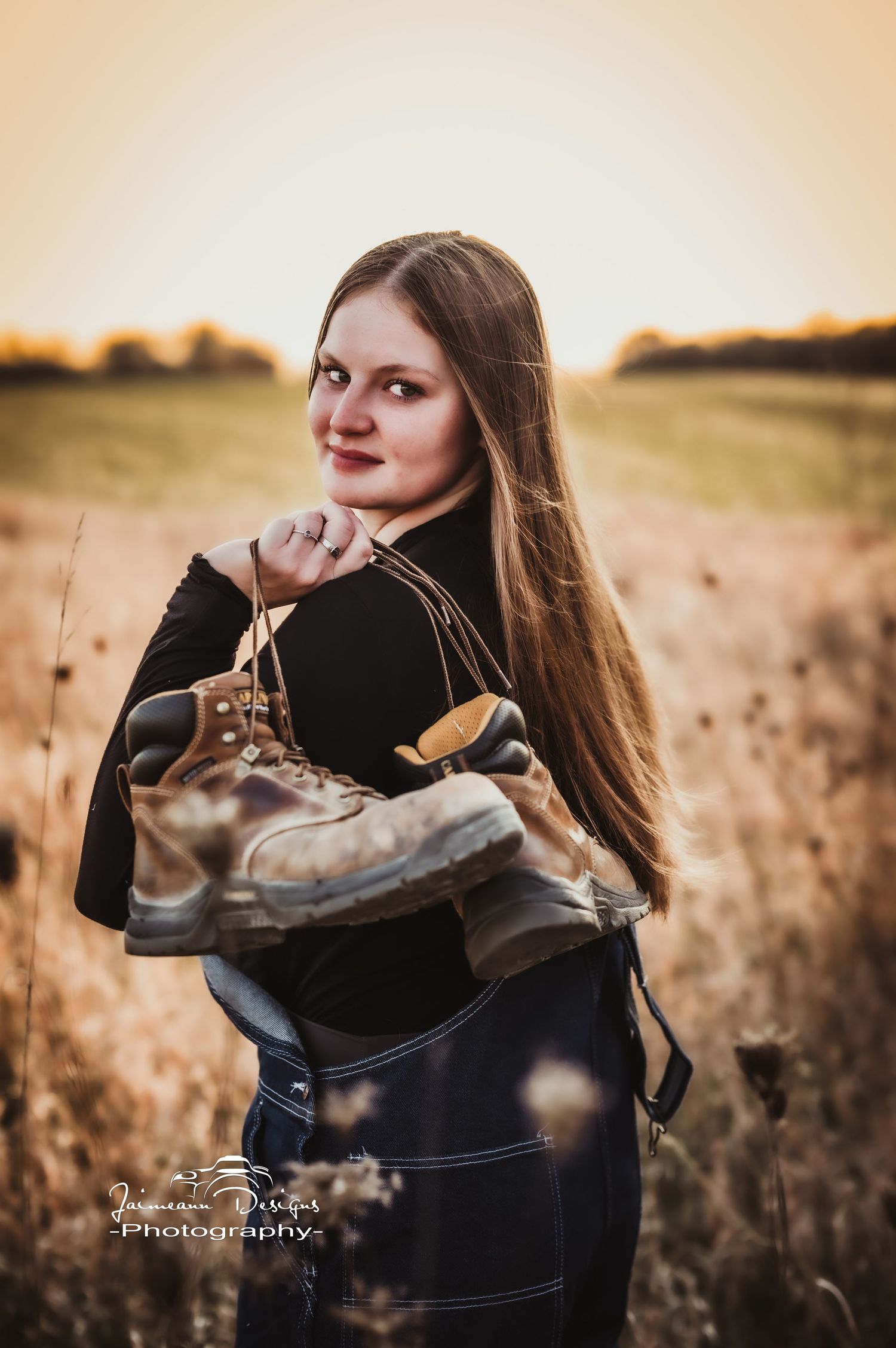 Outdoor fashion portrait in field holding hiking boots during sunset.